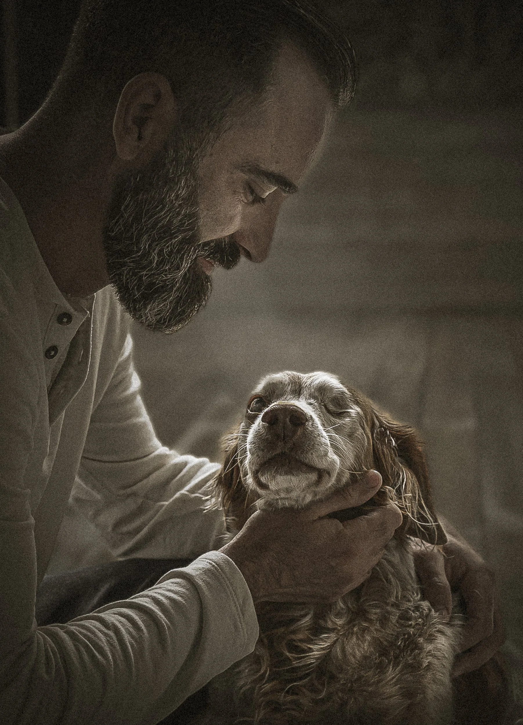 Un homme avec une barbe tient une chienne à l'air détendu, dans un environnement sombre.