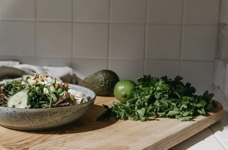 En la mesa hay un plato con ensalada, un aguacate, una lima y un manojo de cilantro