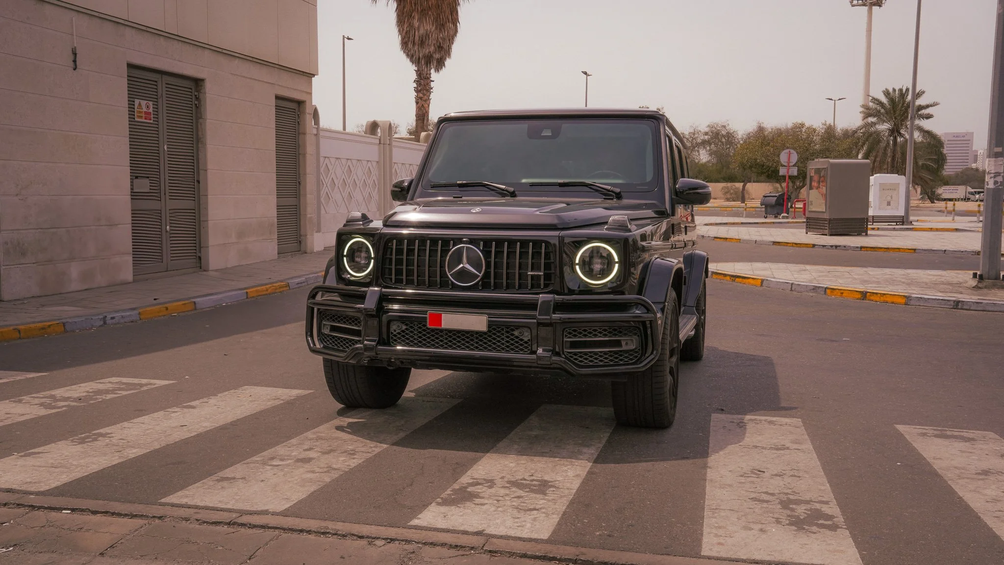 A black Mercedes-Benz G-Class SUV stopped at a pedestrian crosswalk on a city street during daytime.