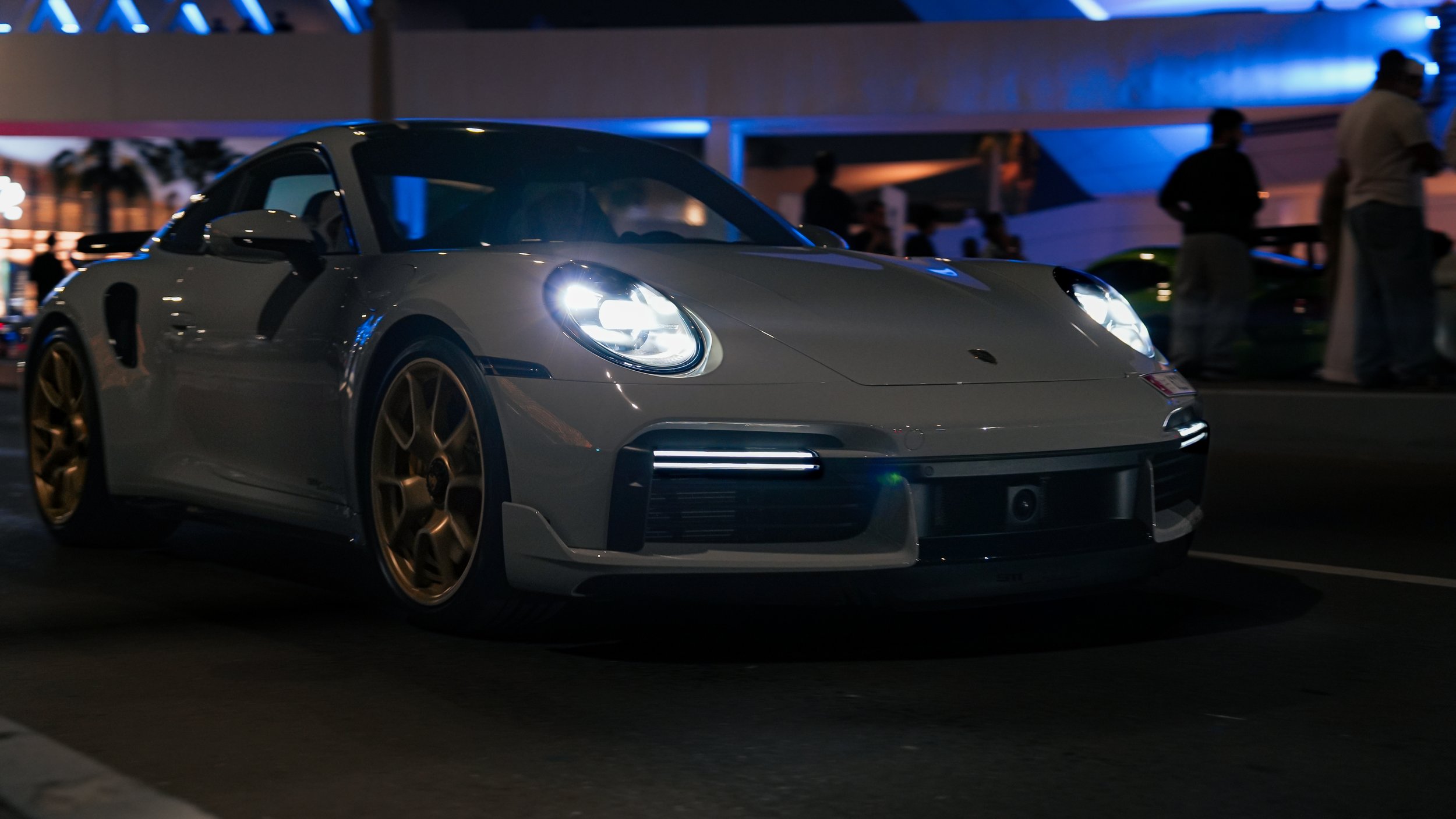 A silver Porsche sports car with gold rims on display and on the go.