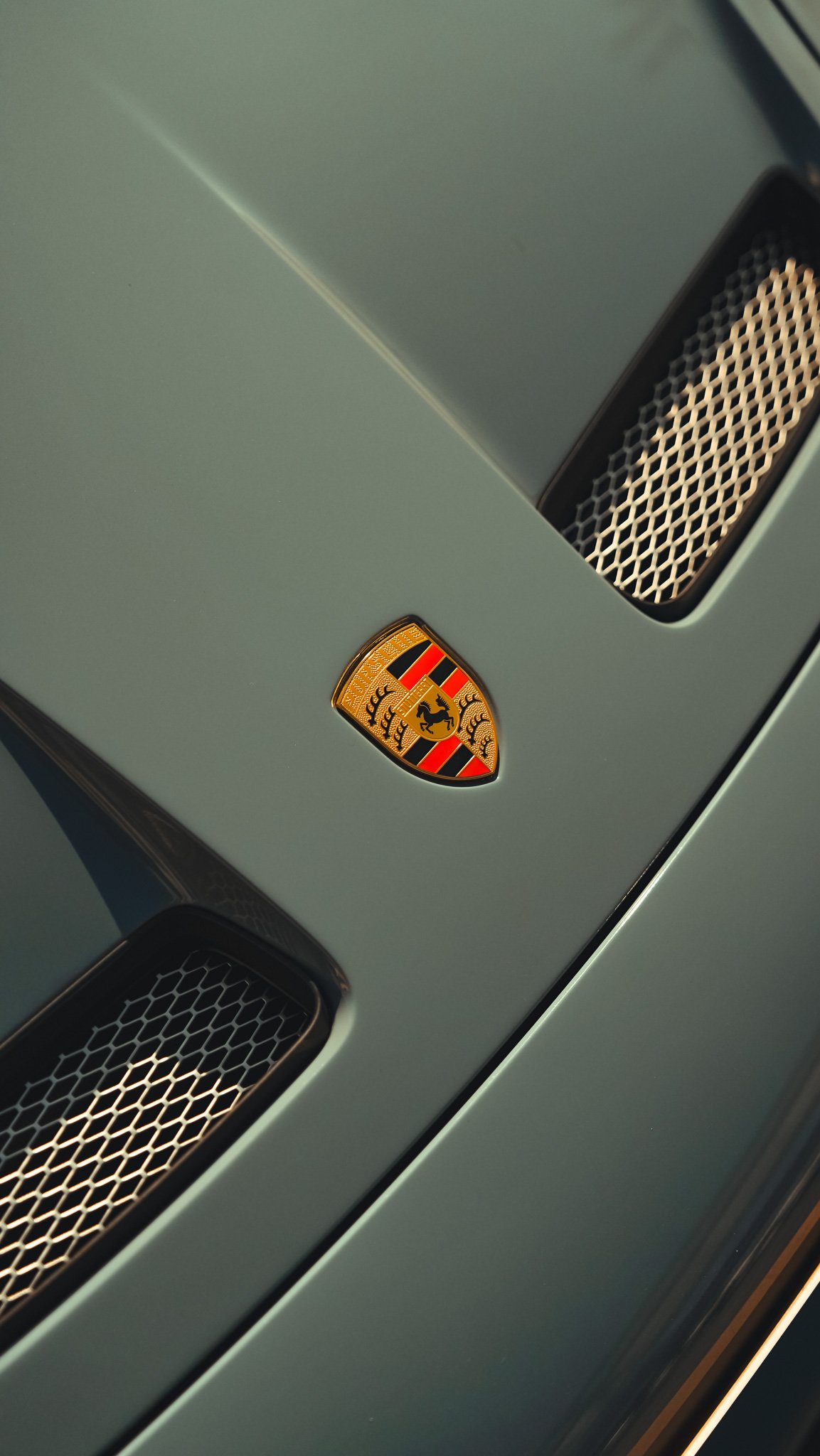 Close-up of a silver sports car hood with a Porsche emblem and dual air vents.