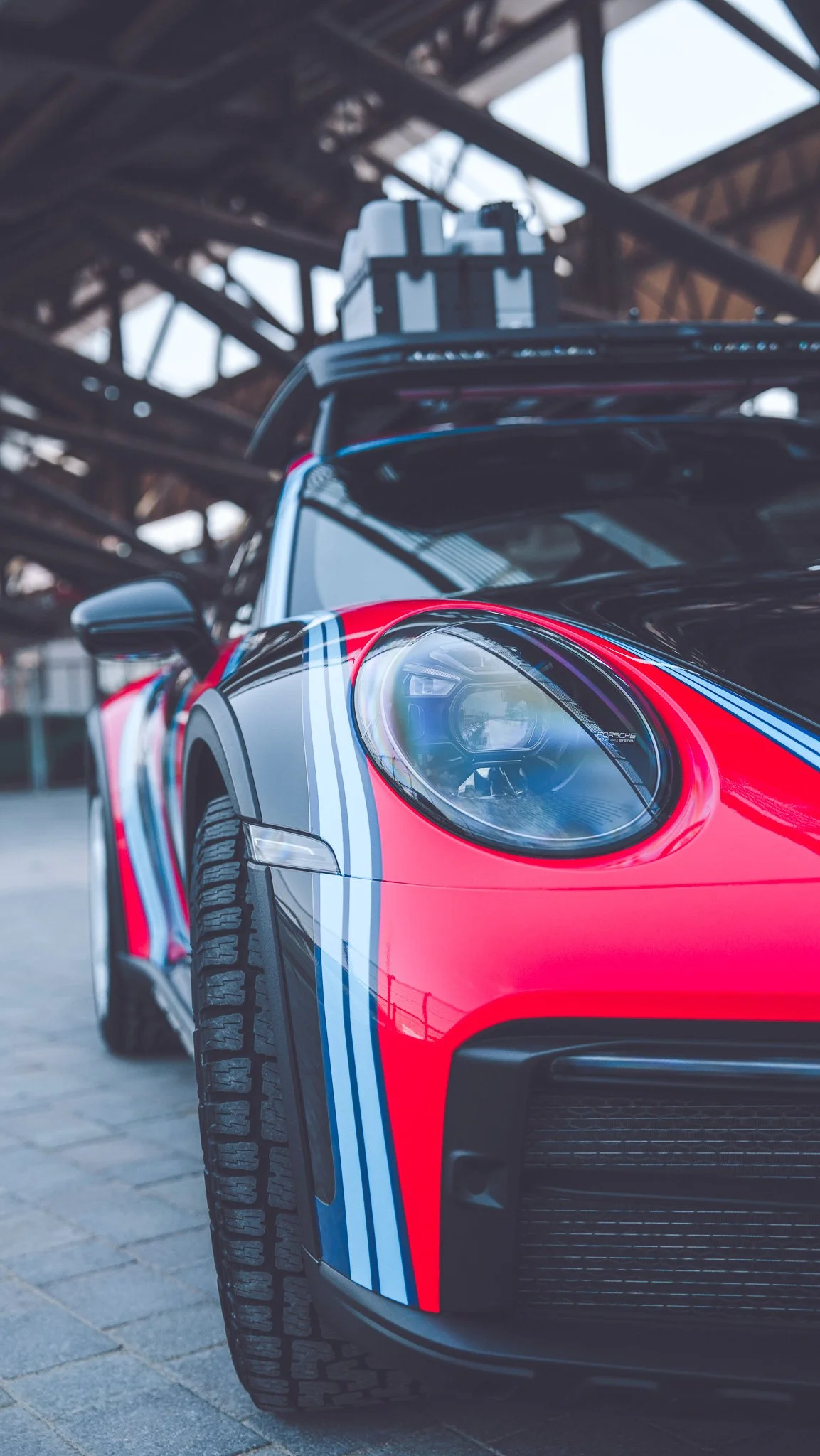 Close-up of a black and red Porsche sports car with blue and white racing stripes under a metal bridge.