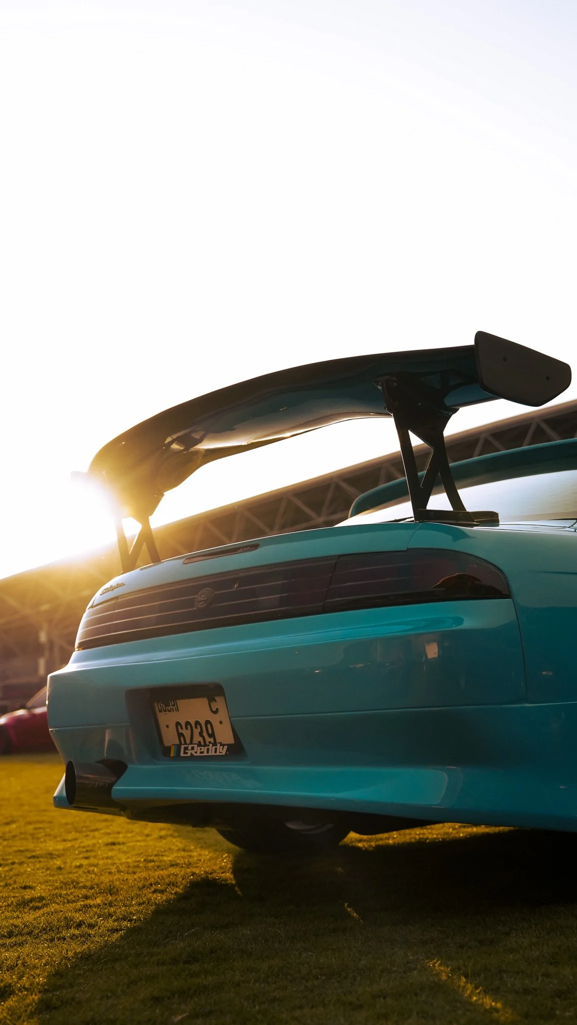 A blue sports car with a large rear spoiler parked on grass during sunset.