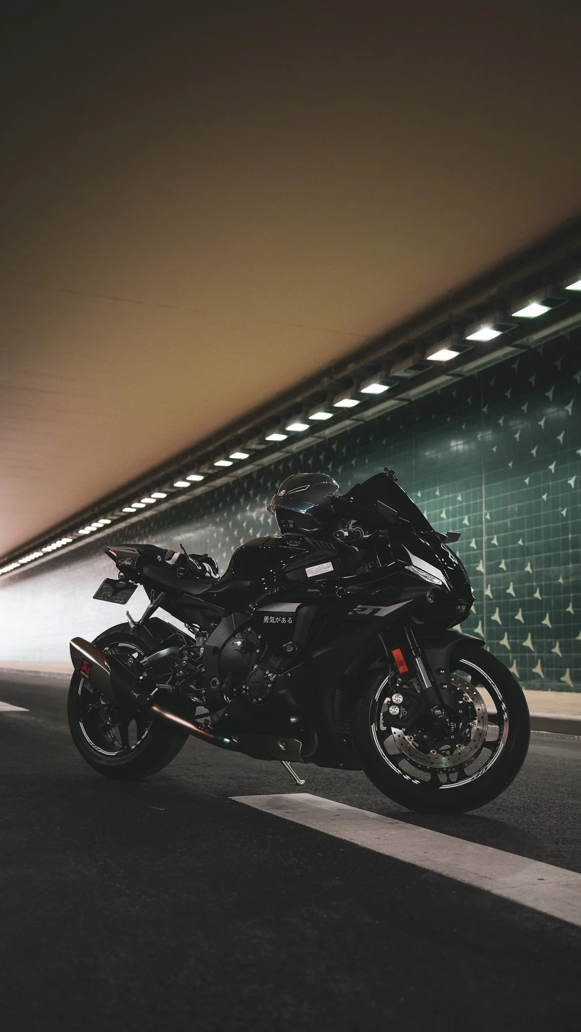 A black sports motorcycle parked in an underground tunnel with a green tiled wall and ceiling lights.
