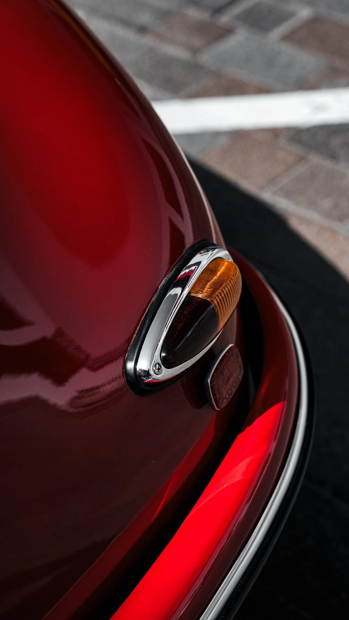 Close-up of the rear end of a red vintage Volkswagen Beetle, showing the tail light, chrome trim, and part of the bumper with a reflective surface.