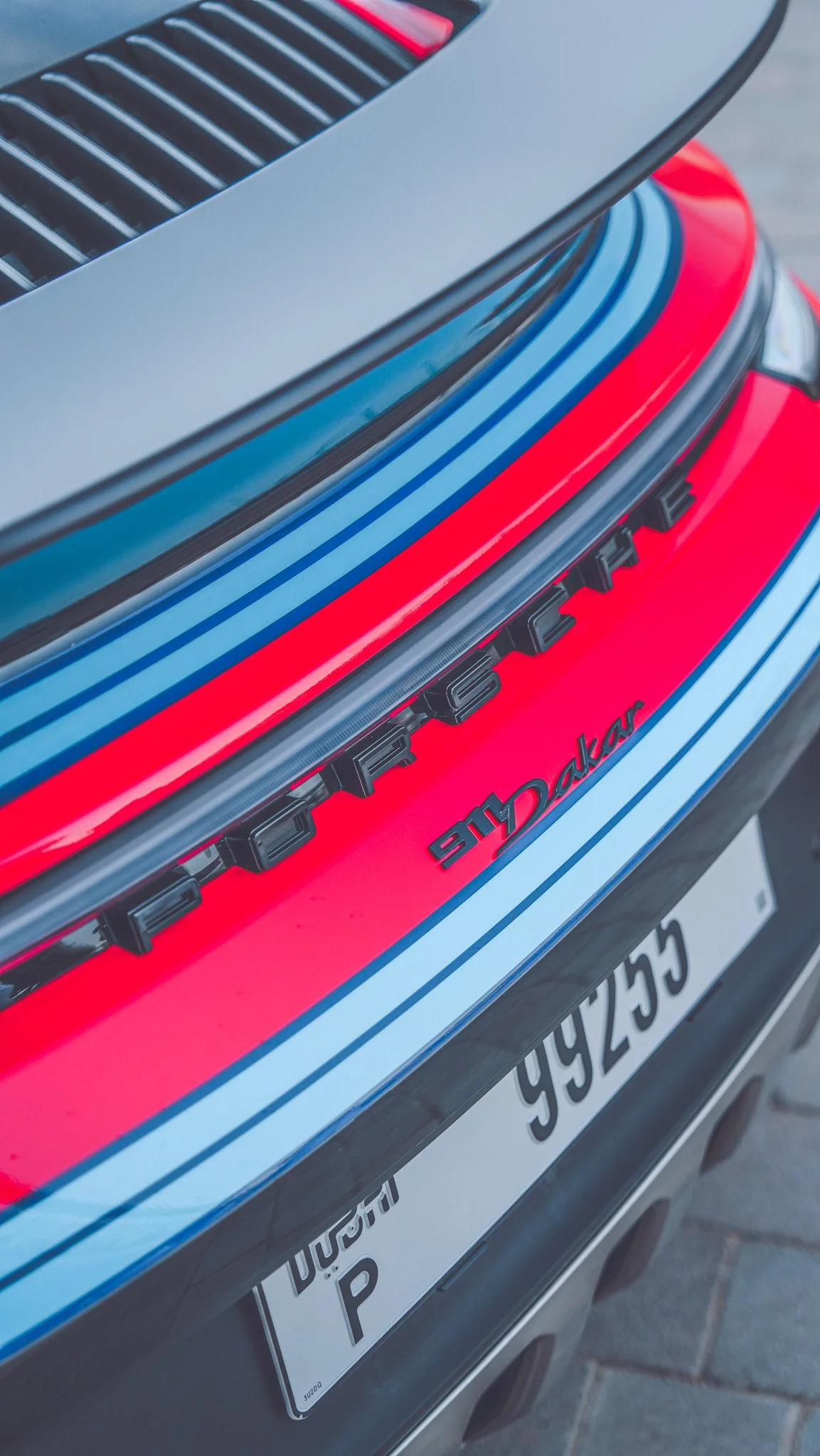 Close-up of a red and blue Porsche car, showing the rear with the Porsche logo and a license plate with the word 'Porsche' and some numbers.