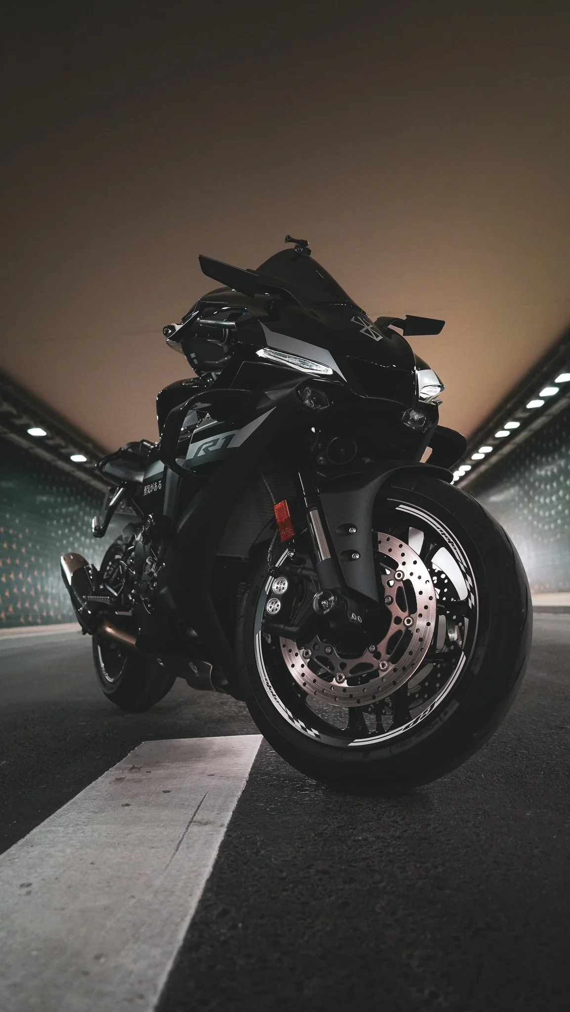 A black sports motorcycle parked in an underground tunnel or parking garage, with a white line on the ground indicating a parking space, and dim lighting from above.
