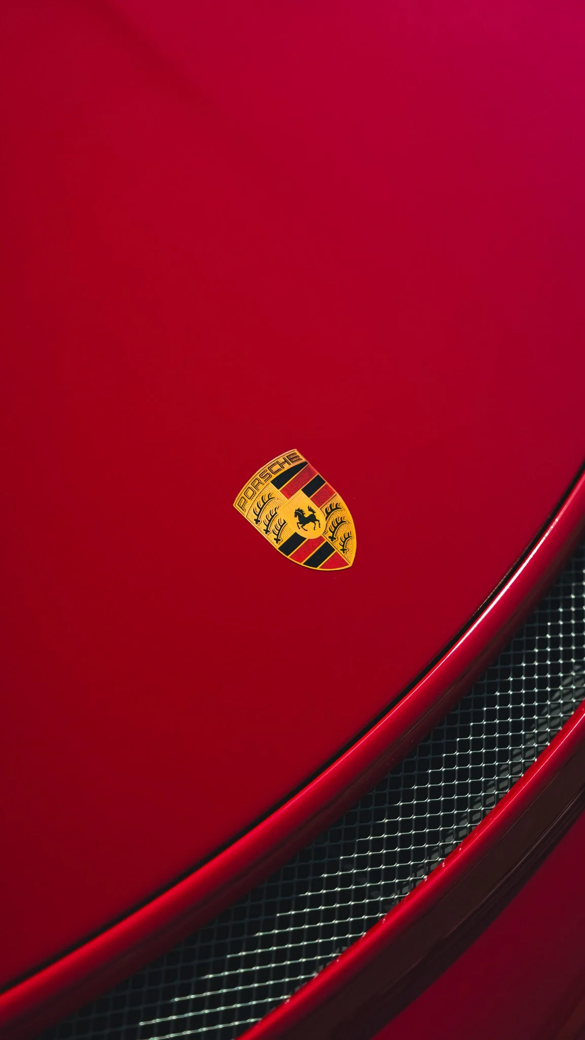 Close-up of the hood of a red Porsche car with a Porsche emblem and a part of the front grille.