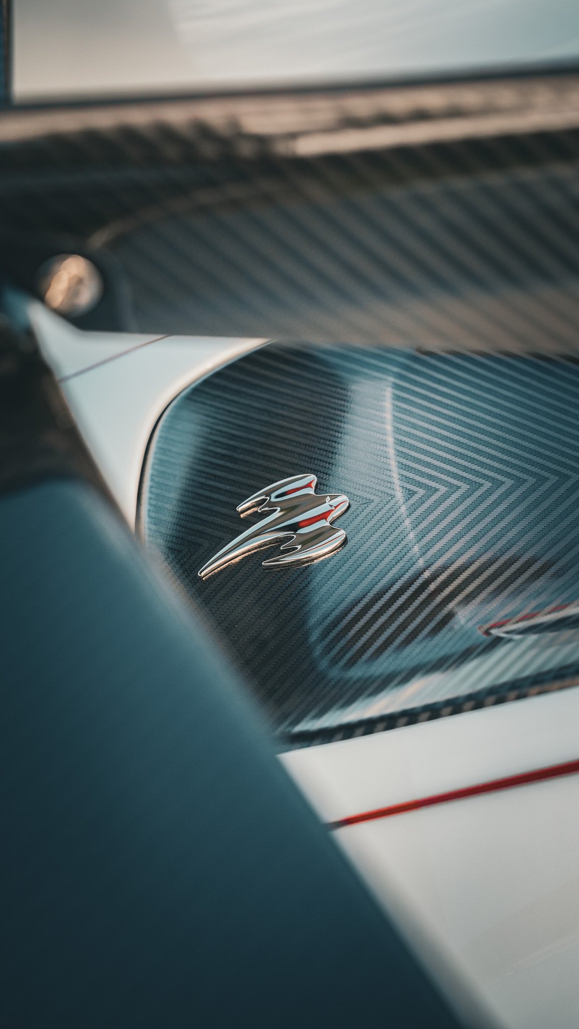 Close-up of a metallic emblem on a carbon fiber surface of a sports car, with blurred background.