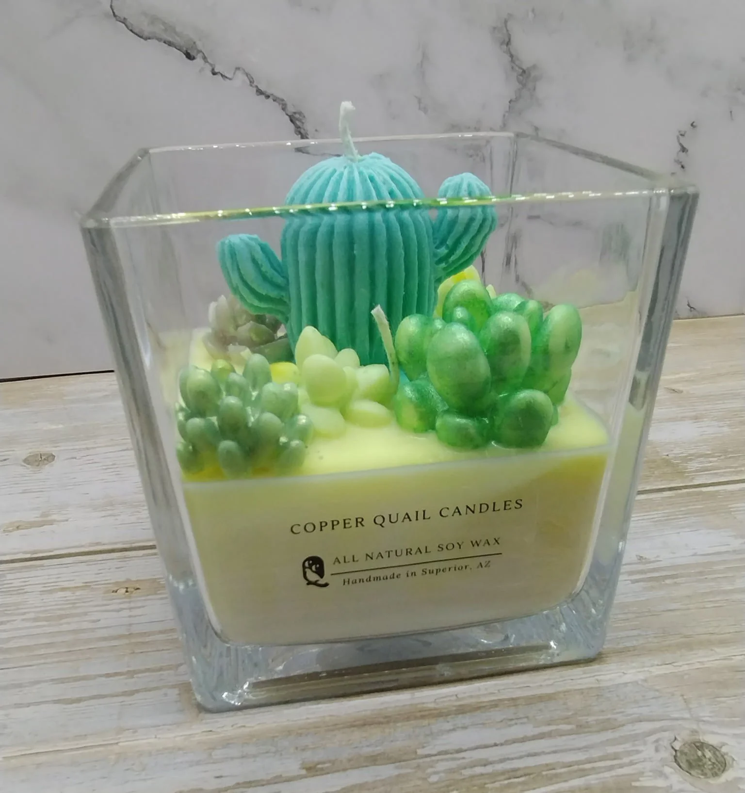 candle with colorful cactus and succulent shapes on top in a square glass container