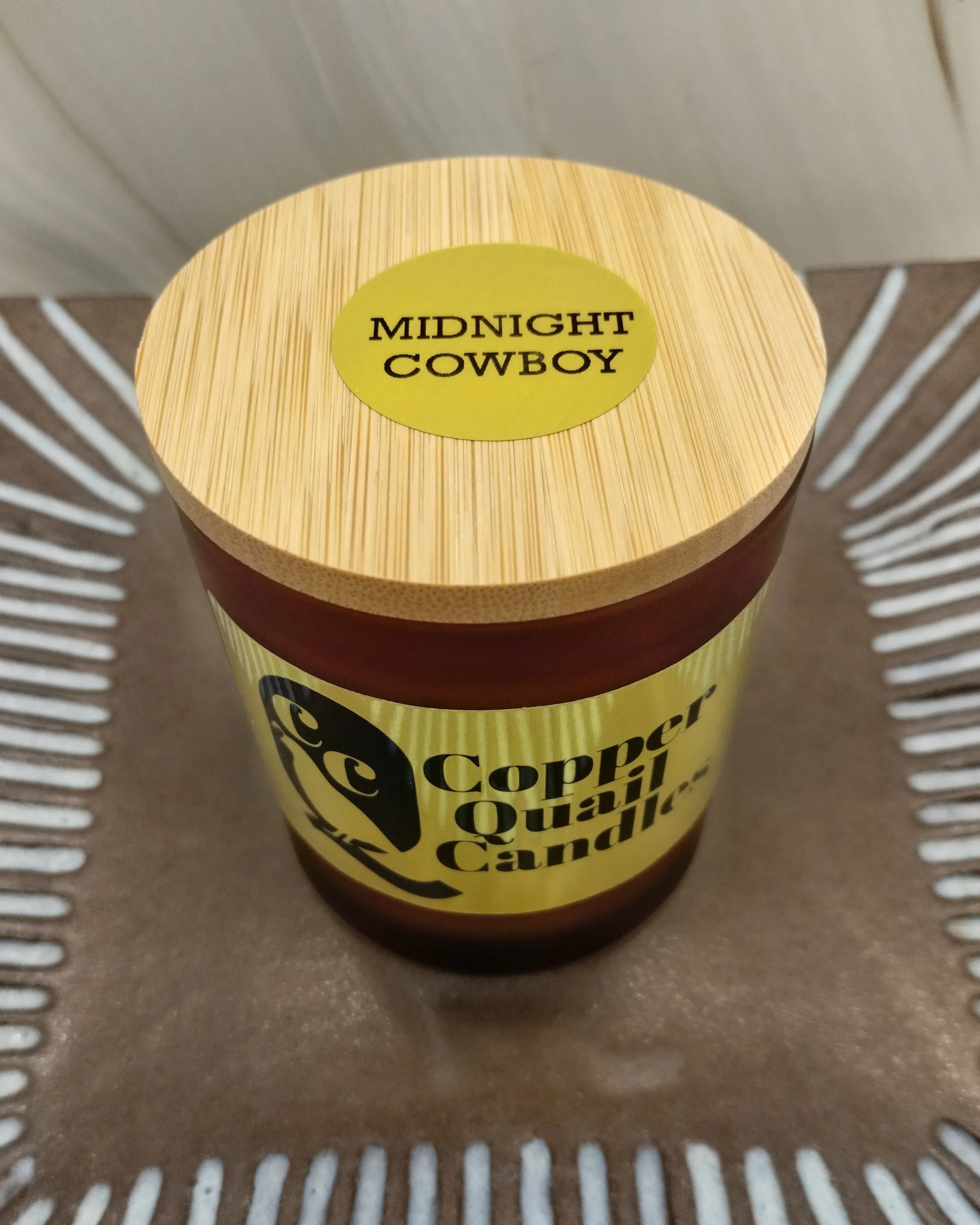 Candle in an amber jar with a wooden lid on top. Hand-poured soy candle. Midnight Cowboy fragrance.