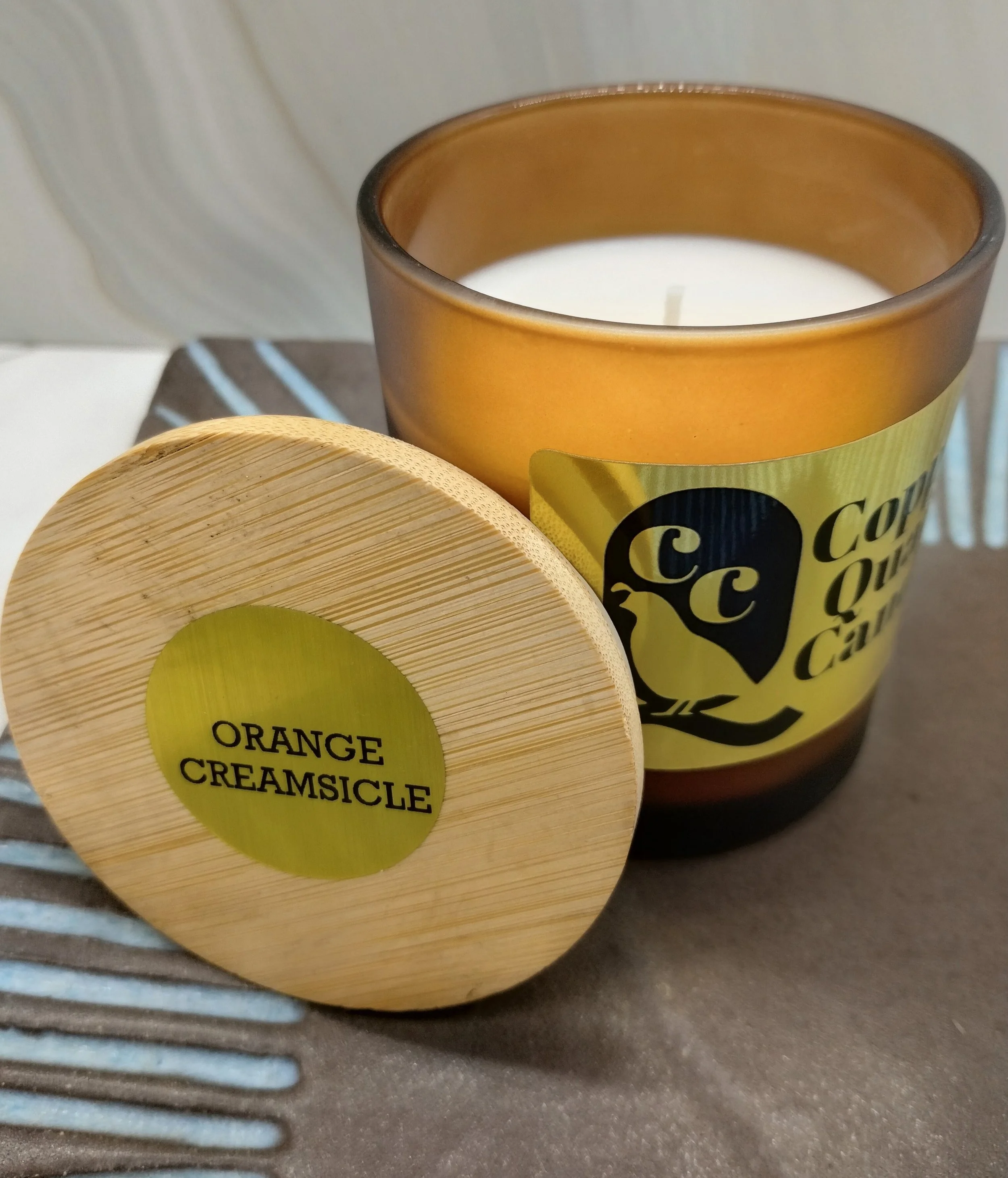 Candle in an amber jar with a wooden lid leaned against it. Hand-poured soy candle. Orange Creamsicle fragrance.