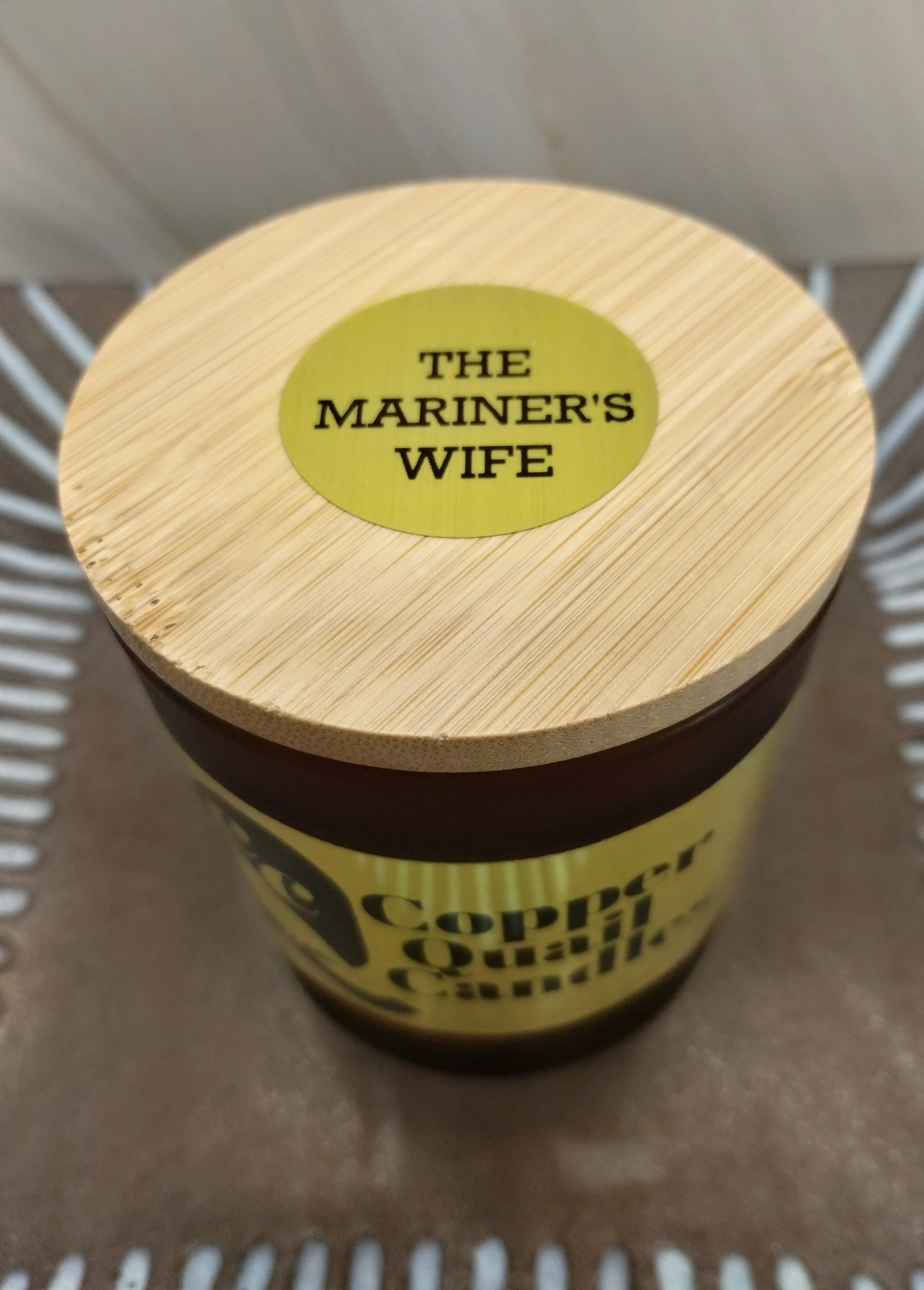 Candle in an amber jar with a wooden lid on top. Hand-poured soy candle. The Mariner's Wife fragrance.