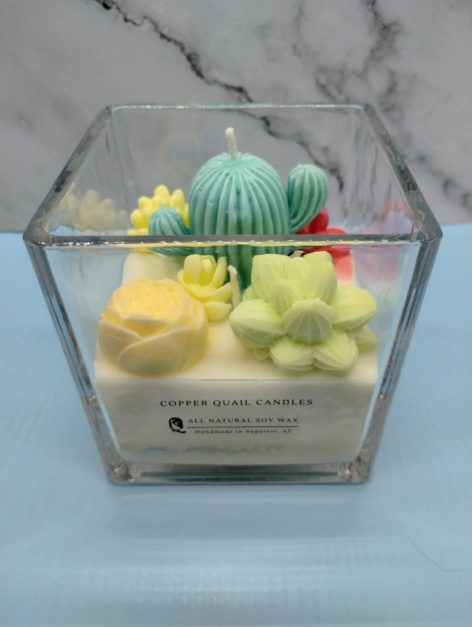 candle with colorful cactus and succulent shapes on top in a square glass container