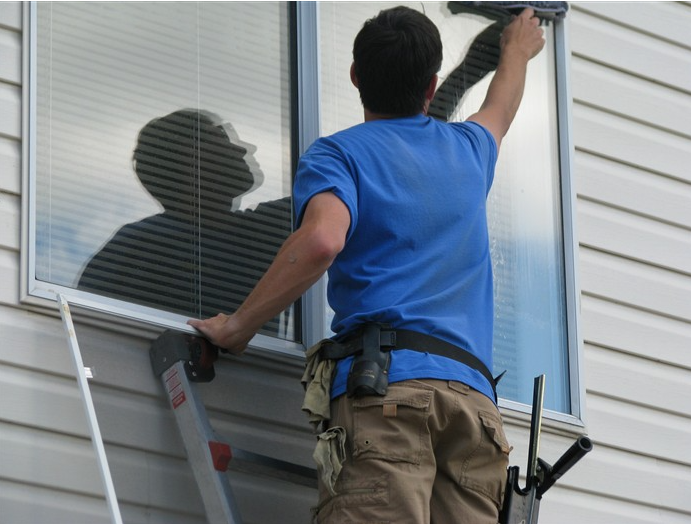 A man installing or repairing a window on the exterior of a house.