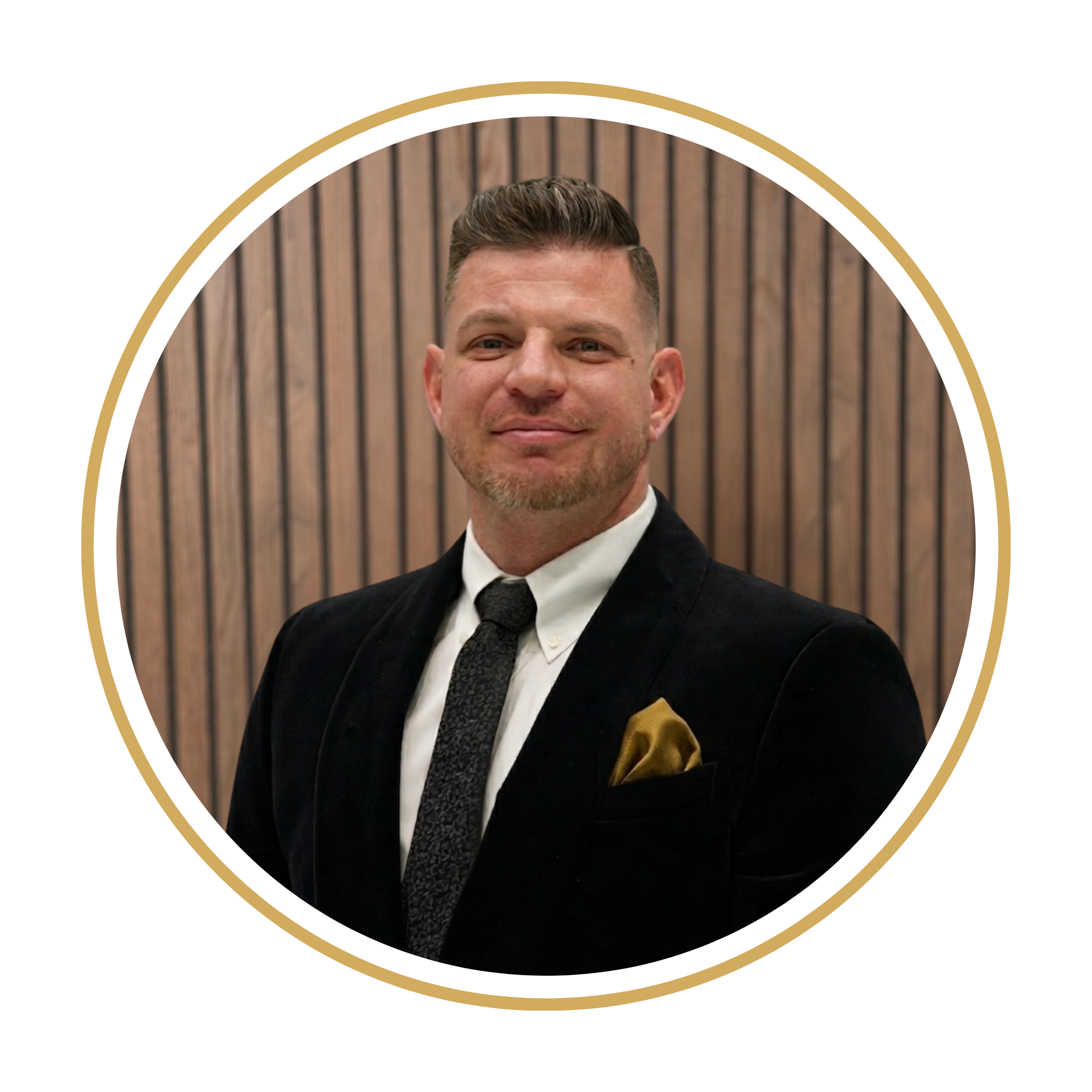Chris with bow tie and gold pocket square smiling against wooden panel background.