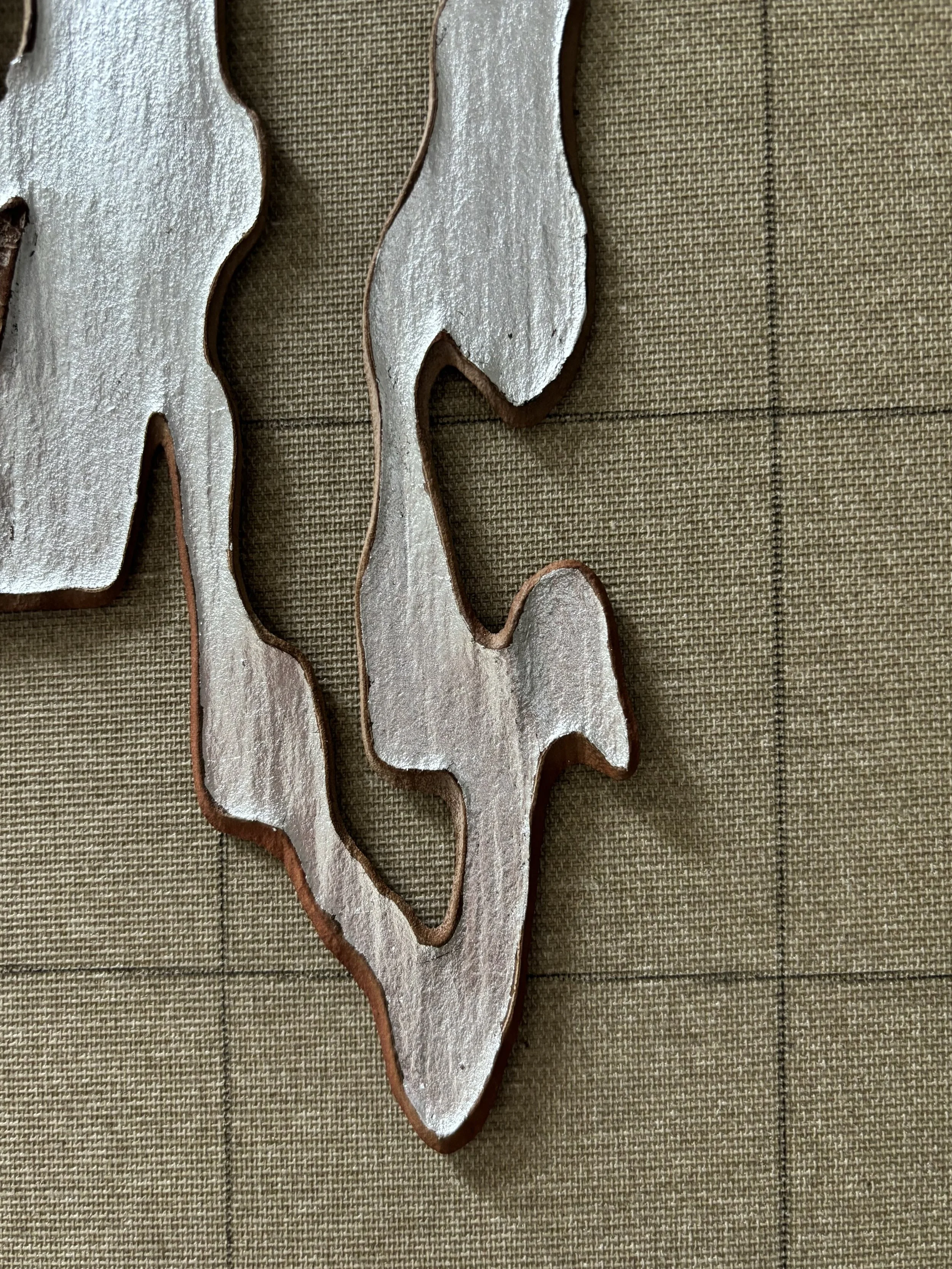 Decorative vintage metal ornament in a leaf or floral shape on a textured, woven background.