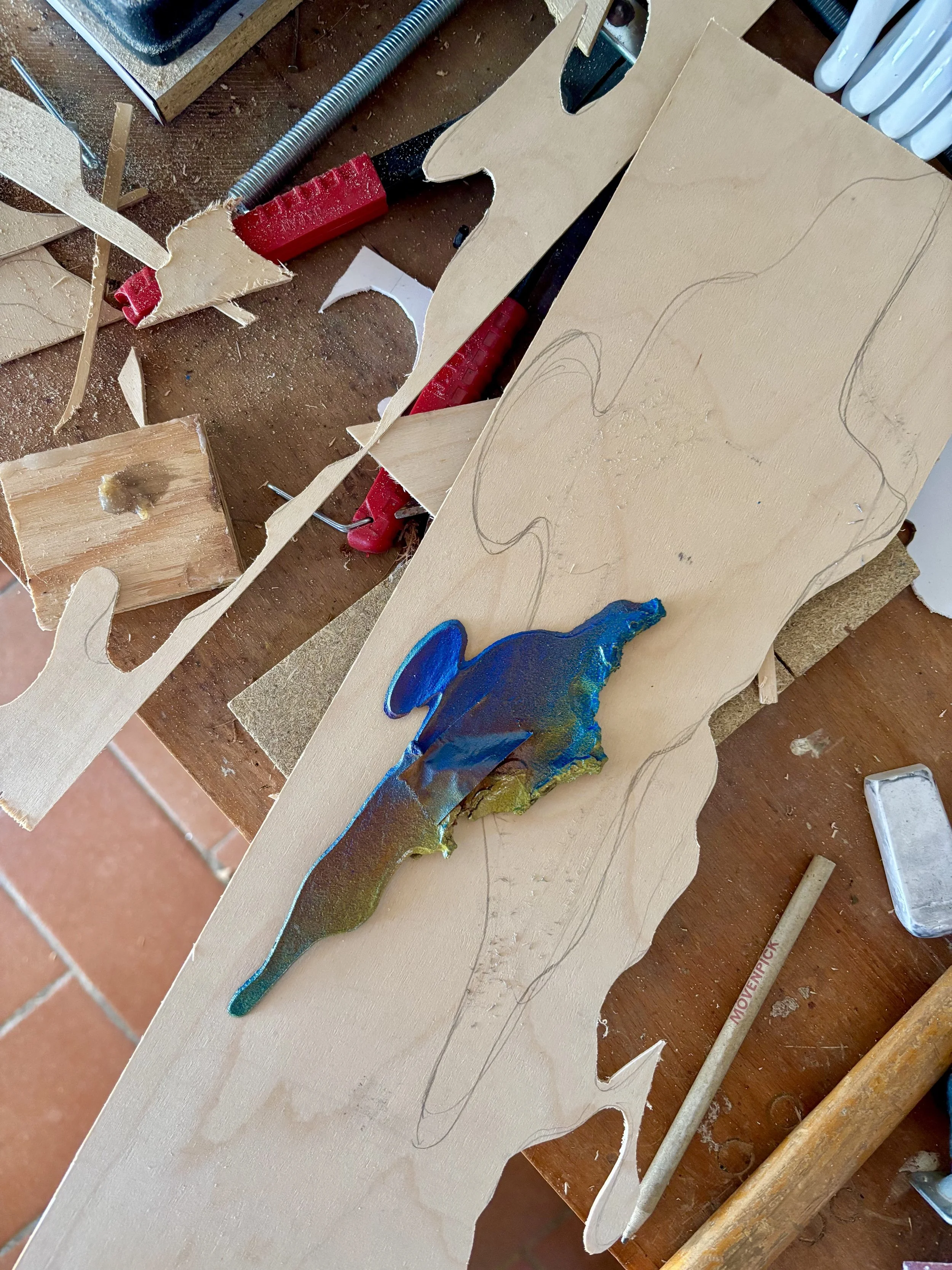 A woodworking workspace with carved paper or wood templates, a file, a pen, and various tools, indicating a craftsmanship or art project in progress.