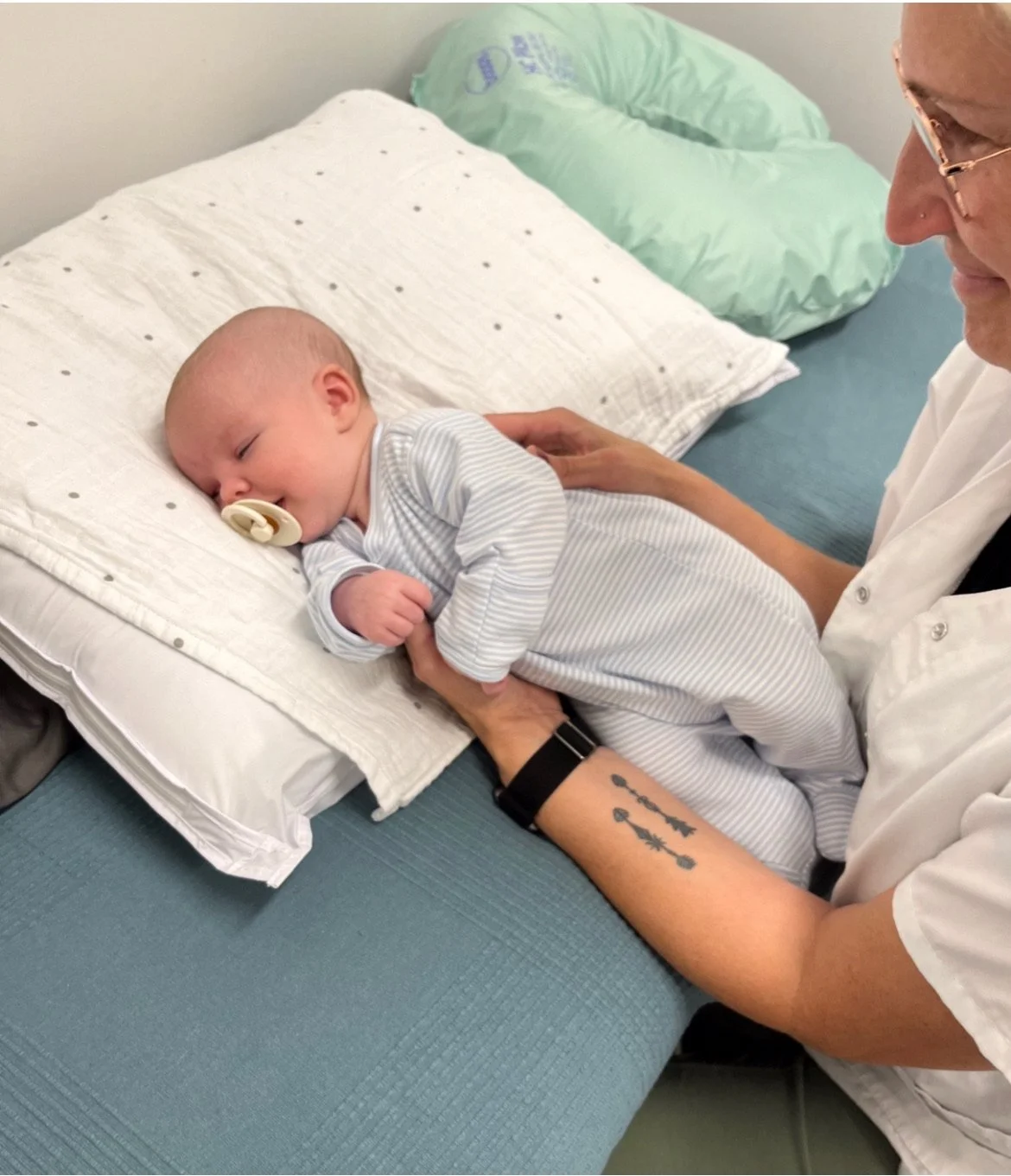 A baby with a pacifier lying on his side on a changing pad, receiving craniosacral therapy.