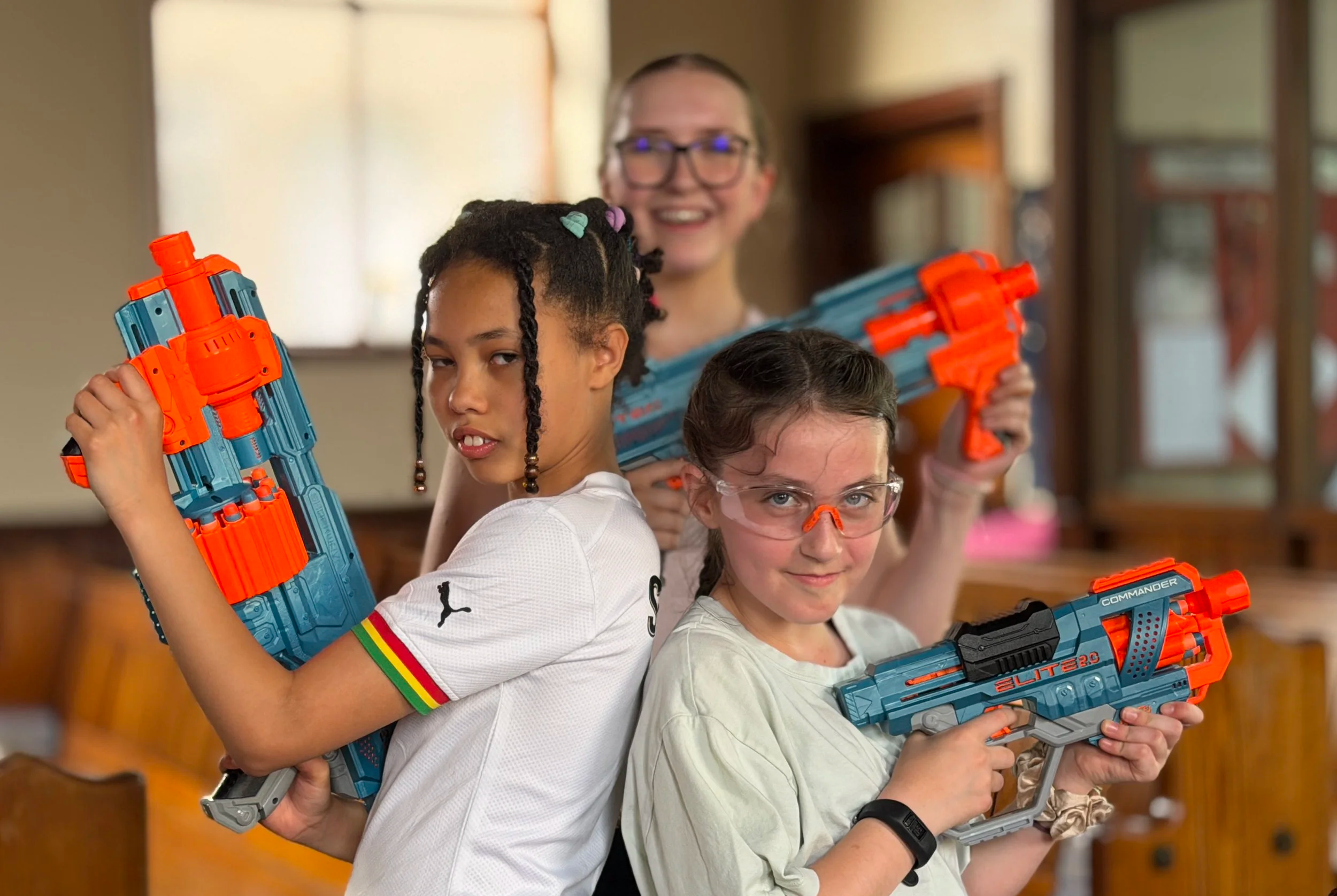 Three children with toy water guns posing inside a room, smiling and looking at the camera.