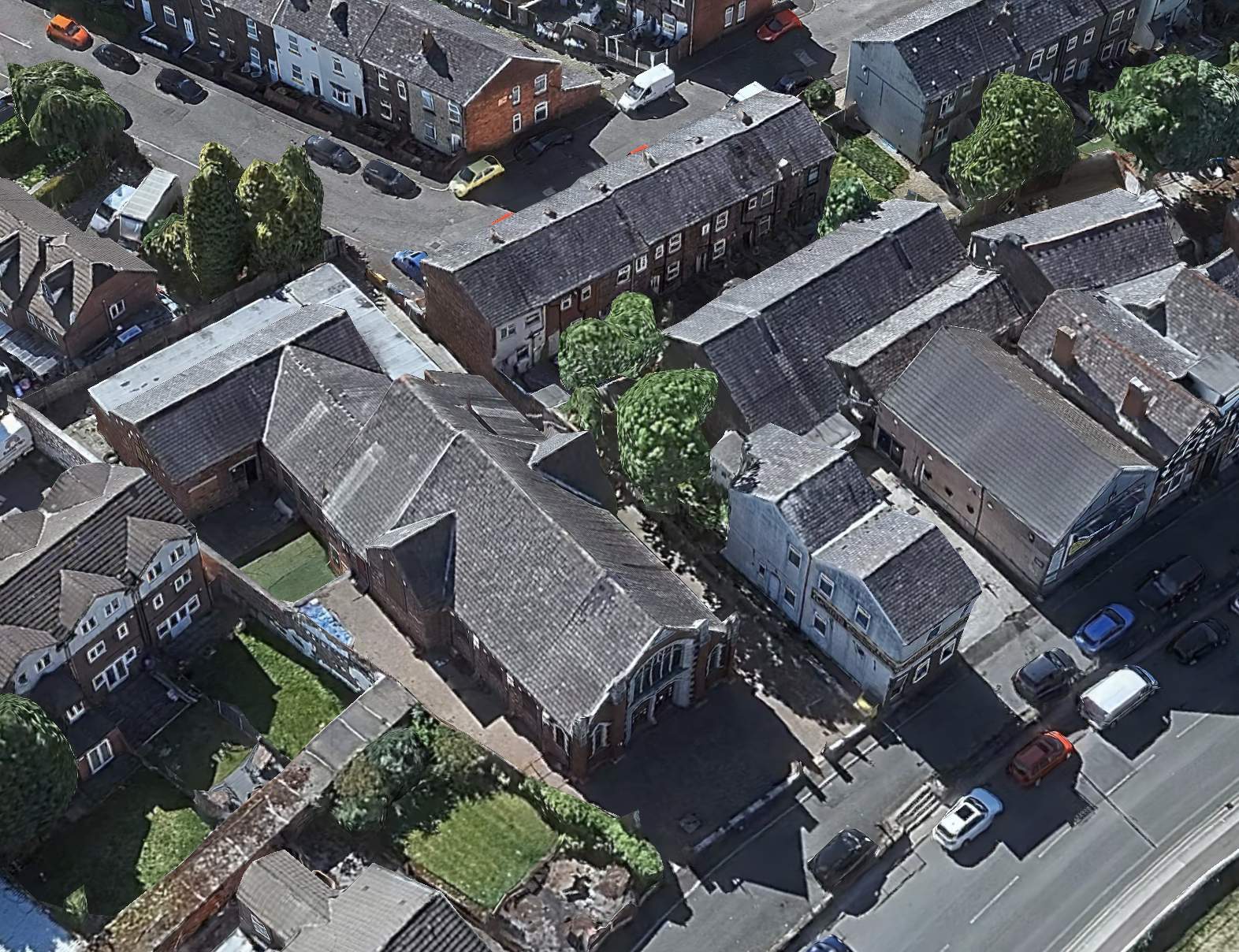 Aerial view of a neighborhood with houses, trees, and parked cars on the streets.