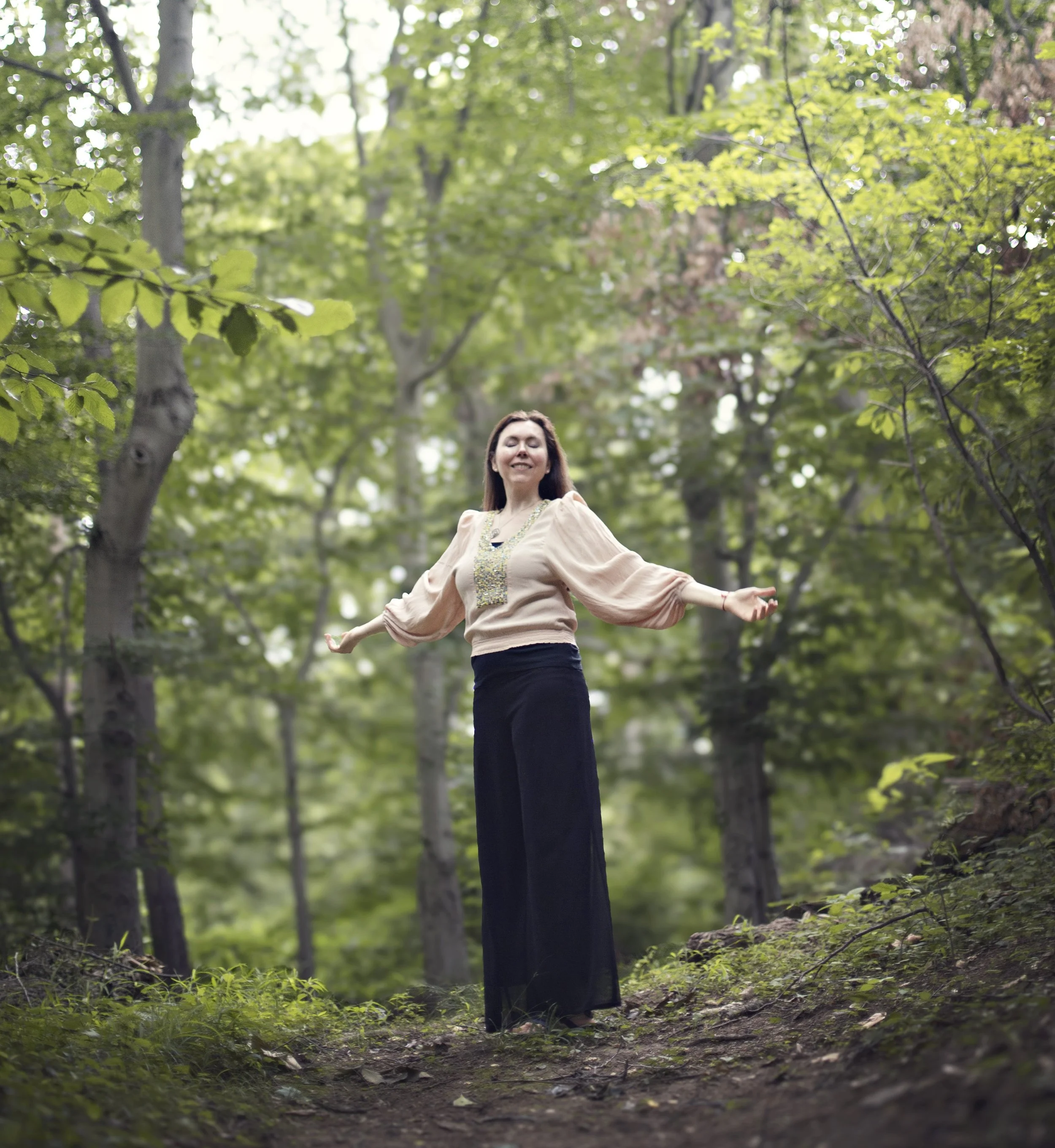 Dr. Lienna Wilson standing outdoors in a forest with arms open and eyes closed, embodying nervous system regulation and grounding in nature.
