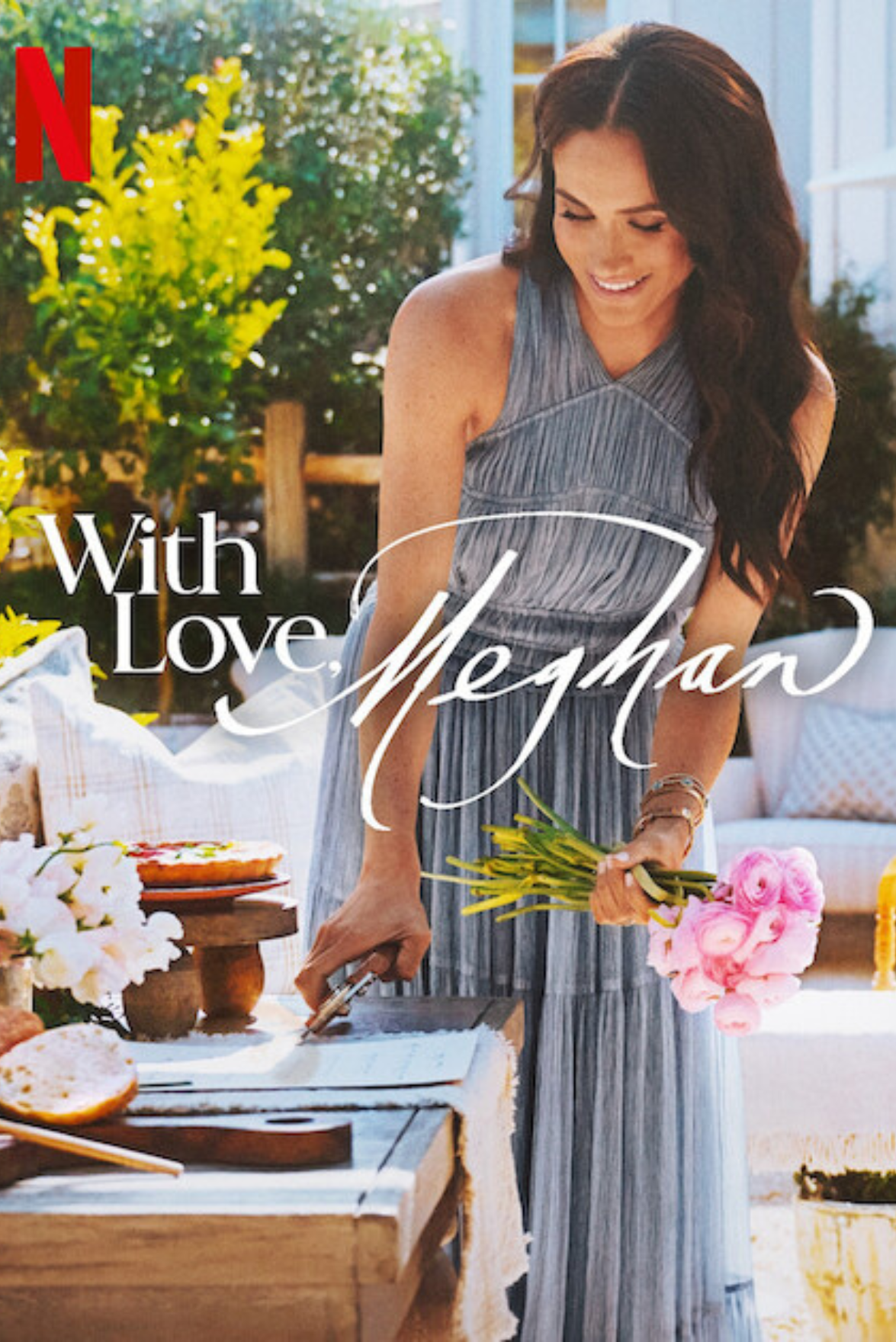 A woman holding pink flowers, smiling, standing outdoors next to a table with food and flowers, with a large green plant in the background, and a message 'With Love, Meghan' overlaid.