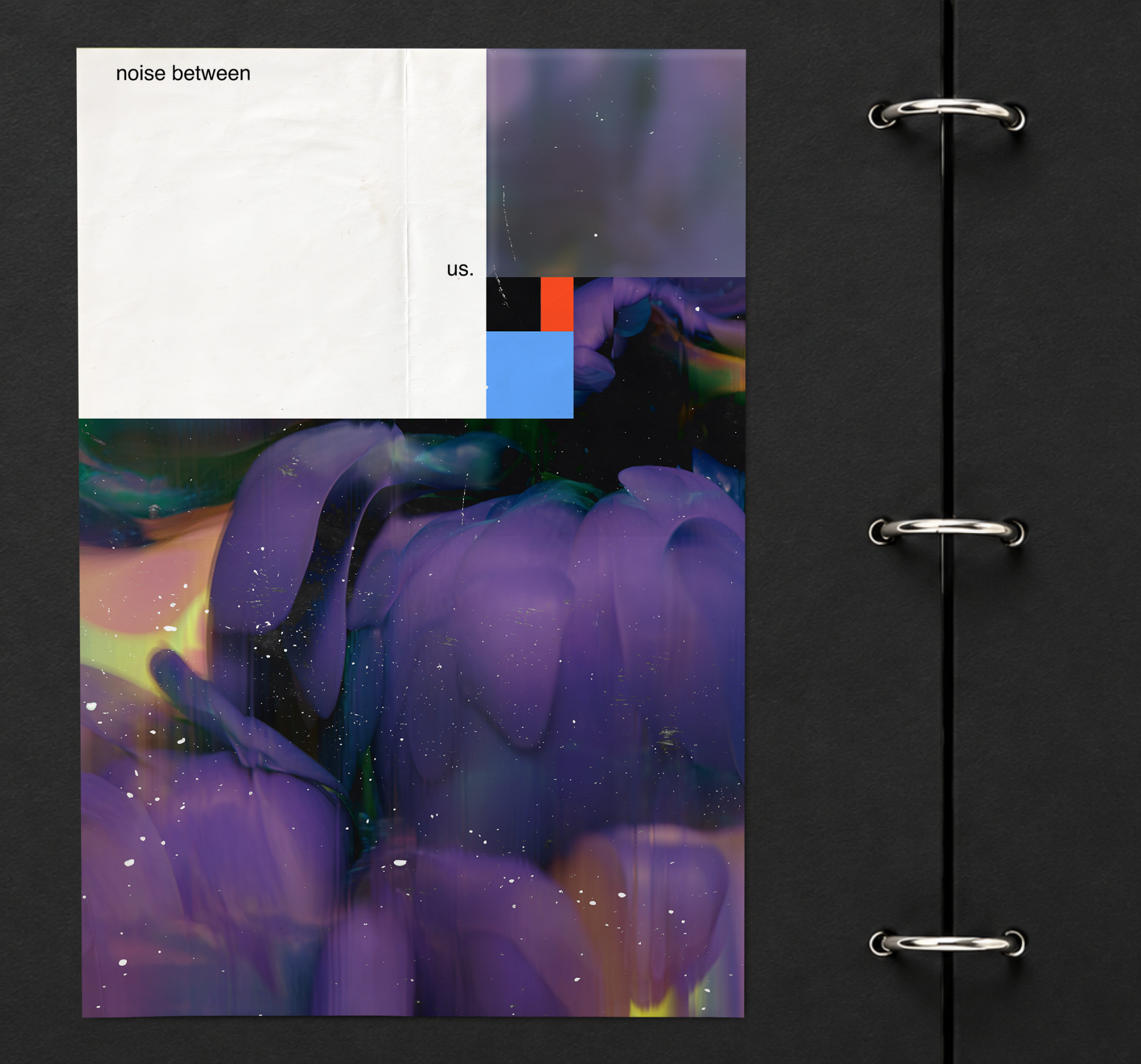 Close-up of an open black binder or album with a printed page inside. The page features an abstract, colorful, cosmic-like artwork with purple, green, and blue hues, and splattered white spots resembling stars. Text on the page reads "noise between us." in the upper left corner.