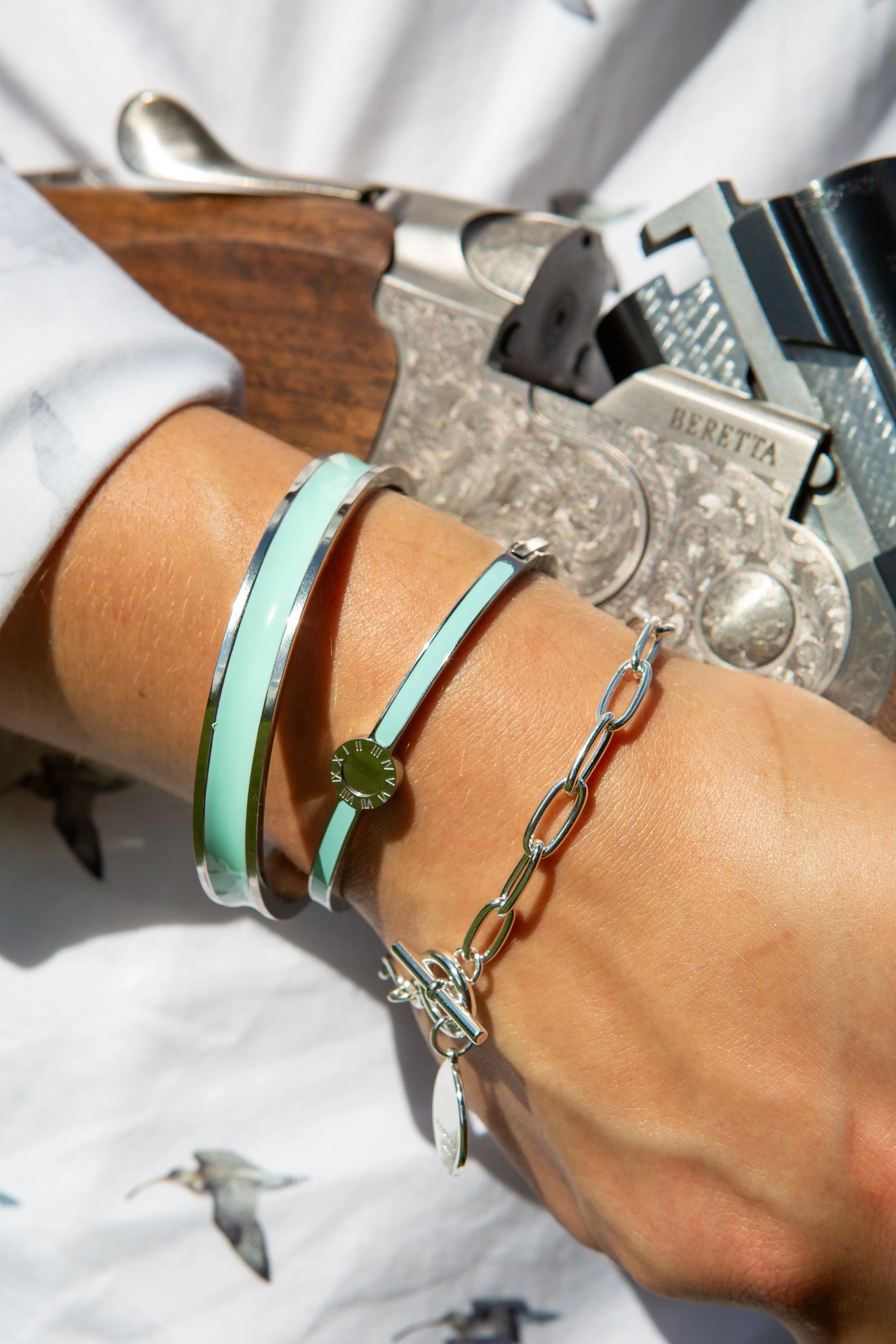 A person with bracelets on their wrist, resting on a surface with a silver Beretta handgun pointed downward nearby.