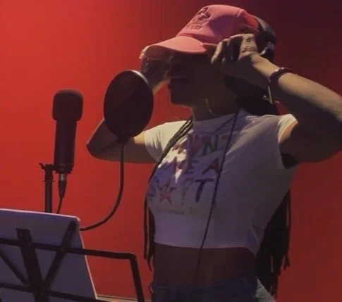 Young woman in a recording studio with a microphone, wearing a pink cap and headphones.