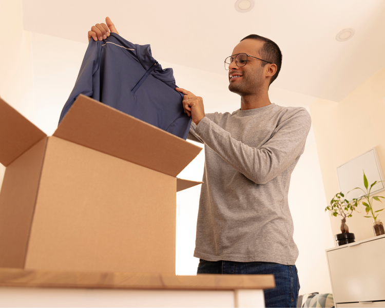 A man smiling as he unpacks clothes from a delivery box at home.