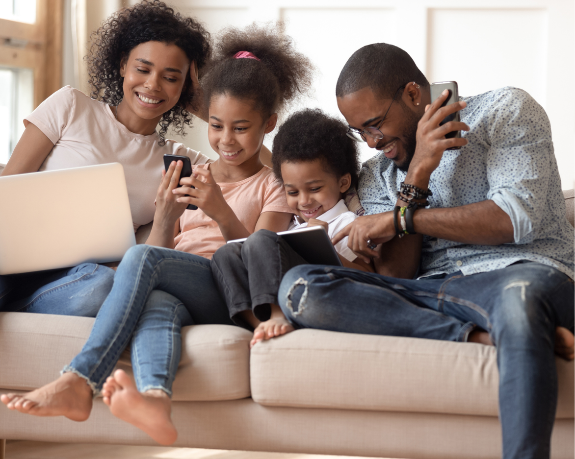A family of four together on a couch — parents and two children — relaxed and laughing.