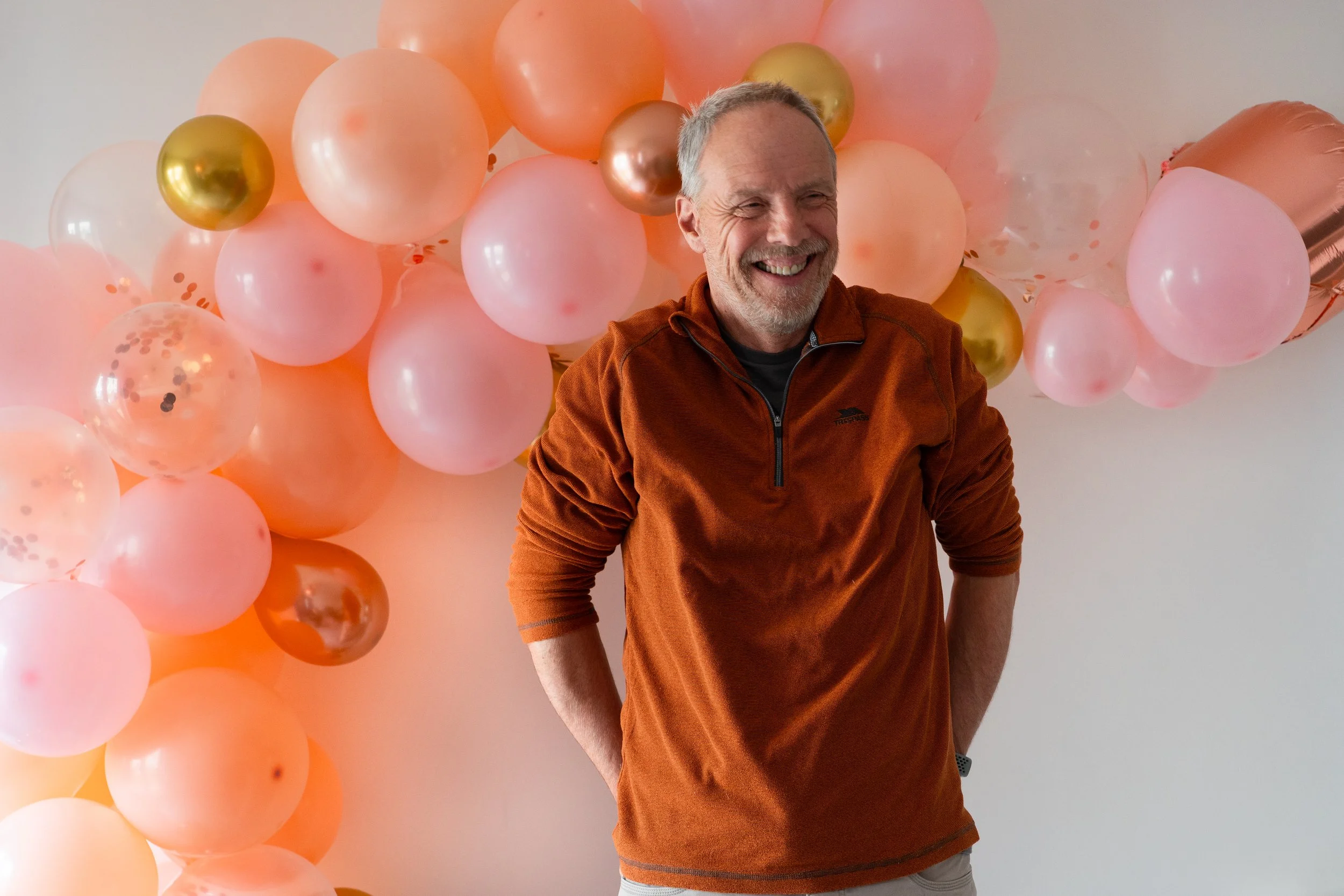 An older family member at the same party smiling happily and genuinely at something off camera. the colour palette is warm toned and complimentary