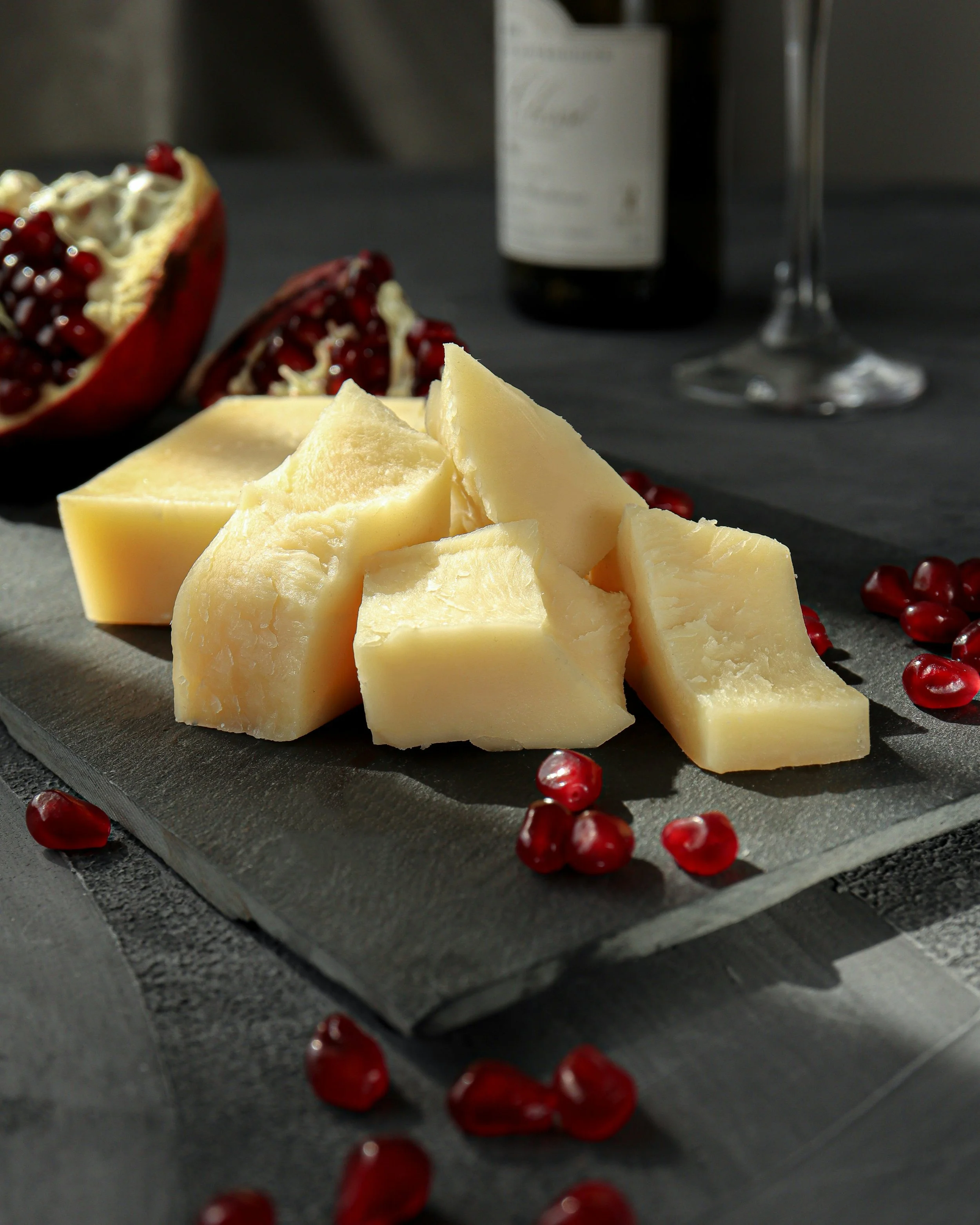 Fromage en morceaux sur une planche en ardoise avec des grains de grenade, une bouteille de vin et un verre de vin en arrière-plan.