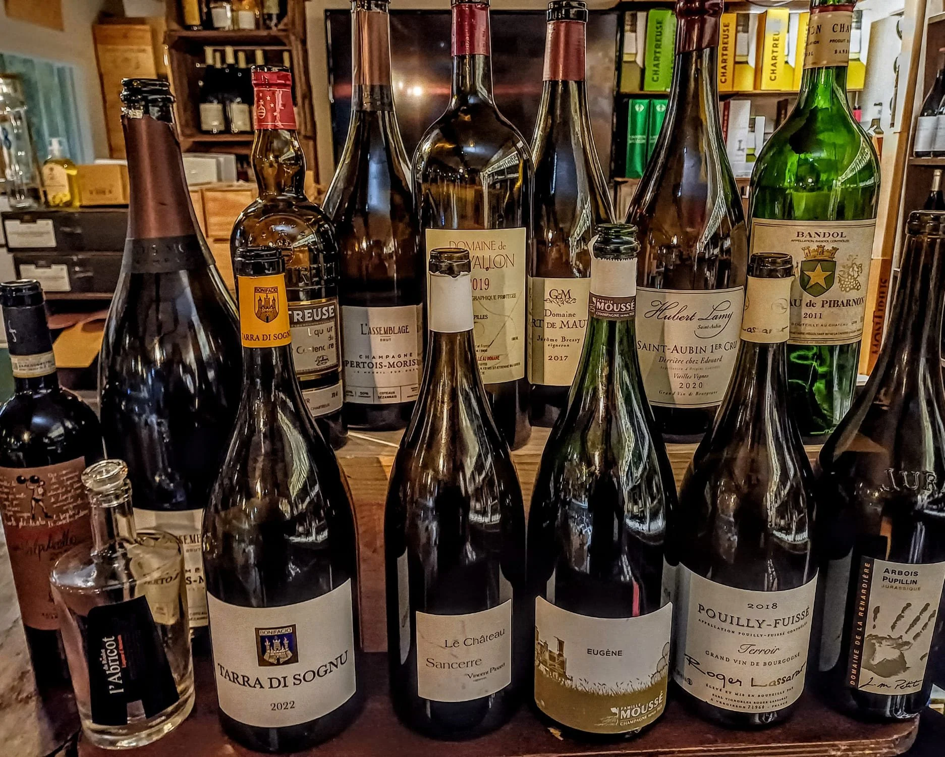 Bouteilles de vin alignées sur une étagère en bois dans une boutique ou un caveau, avec divers étiquettes de vins français.