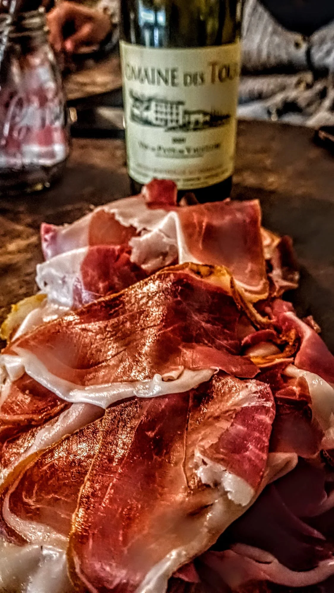 Assortiment de jambon apparemment cru ou séché, posé sur une surface en bois, avec une bouteille en arrière-plan.