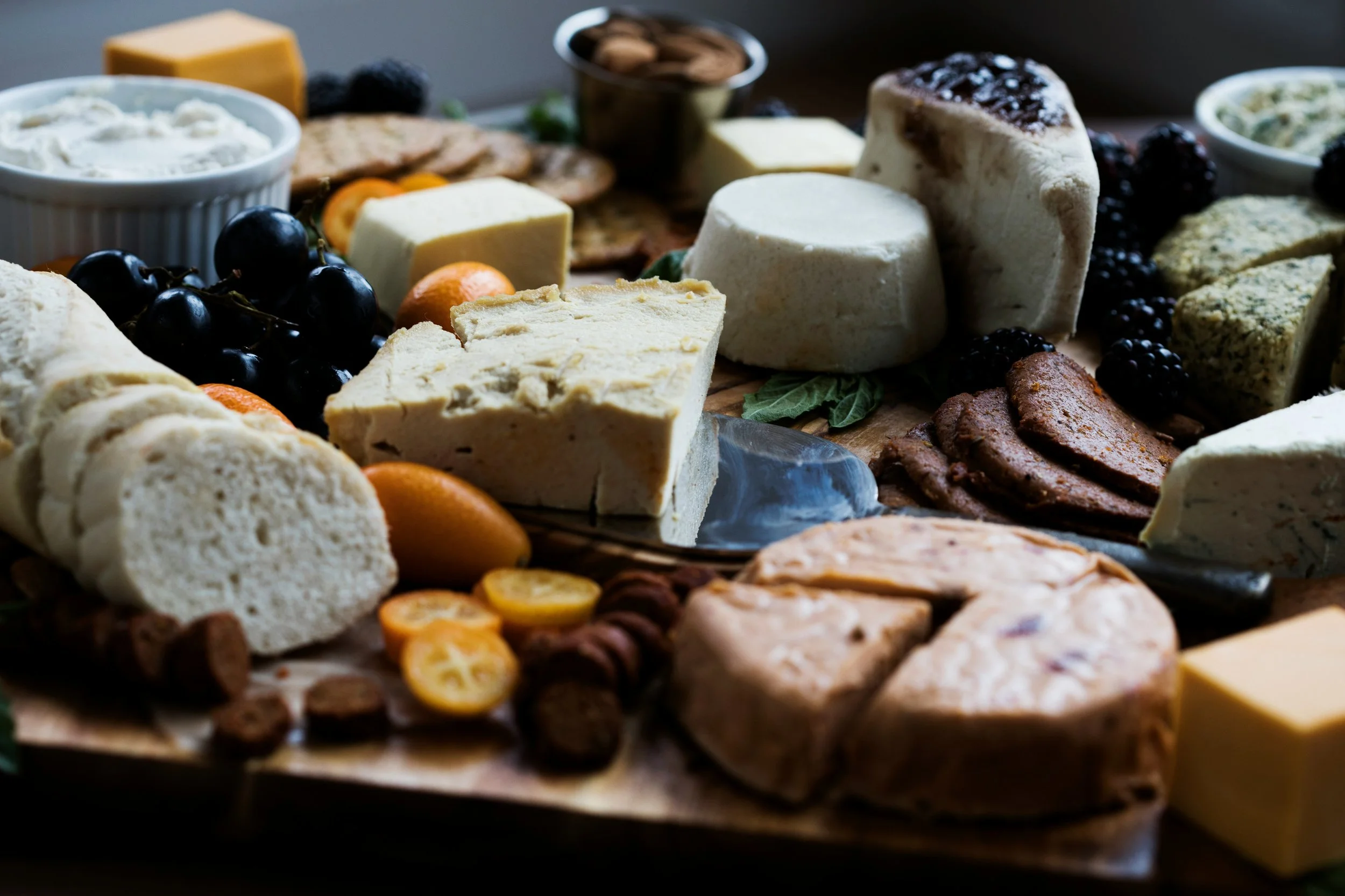 Plateau de fromages variés avec raisins noirs, noix, et morceaux de fruits.