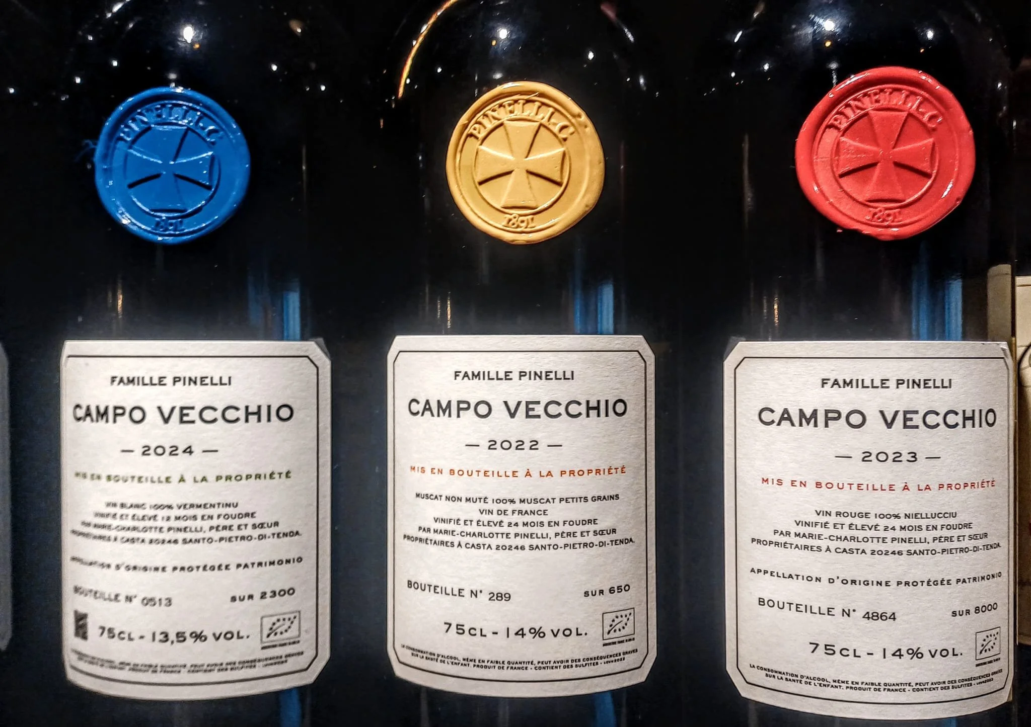 Trois bouteilles de vin avec des étiquettes de la famille Pinelli, indiquant différentes années : 2024, 2022 et 2023, provenant de Campo Vecchio en France.