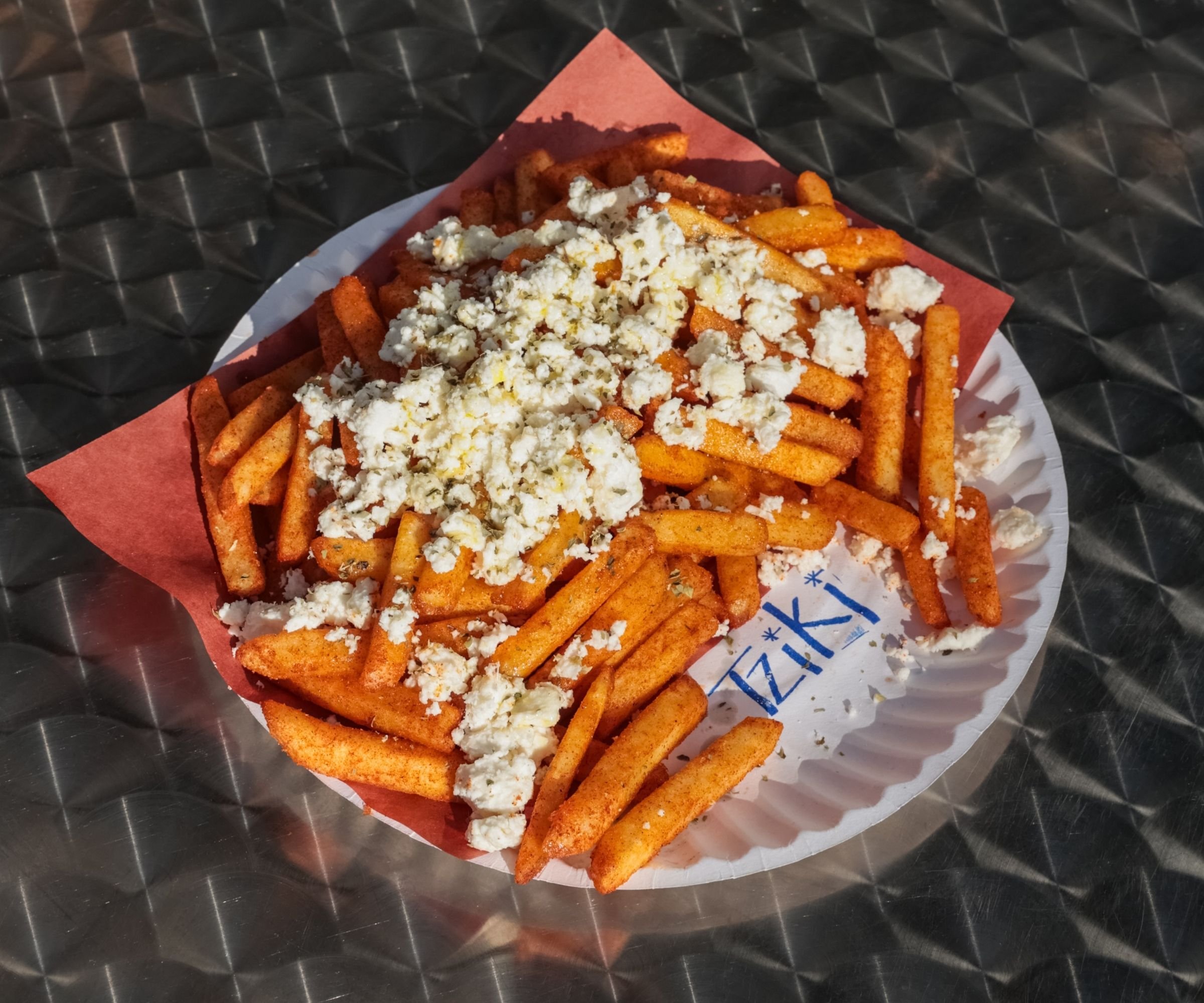 Greek-style hand-cut fries topped with crumbled PDO feta and Greek oregano on Tziki branded paper plate, best Greek souvlaki shop in Chelsea Manhattan NYC