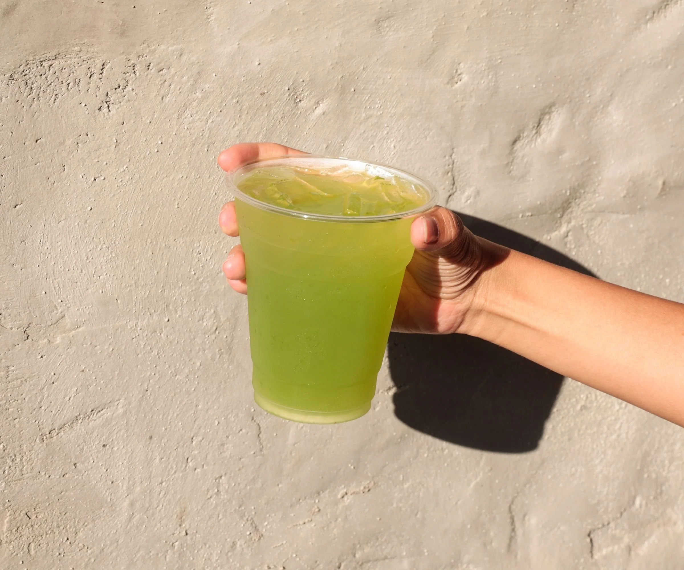 Refreshing cucumber melon mint Greek homemade drink in hand against Tziki stucco wall, best Athenian souvlaki shop in Chelsea Manhattan NYC