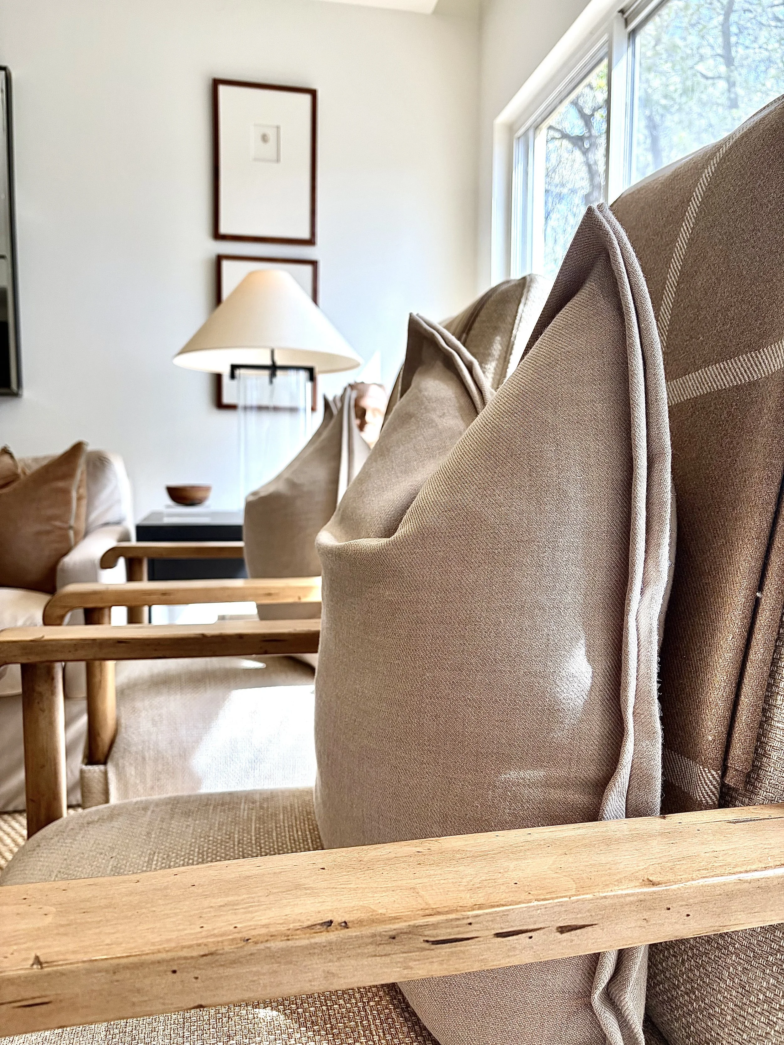 Close-up of beige upholstered armchair with wooden armrest in a living room, with other furniture and artwork in the background.