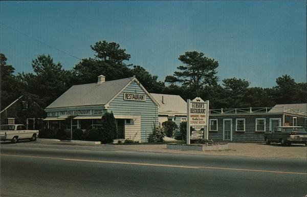 A small restaurant building with a sign that reads 'Tebo's Restaurant' and a larger sign listing menu items outside, situated next to a few parked cars and surrounded by trees under a partly cloudy sky.