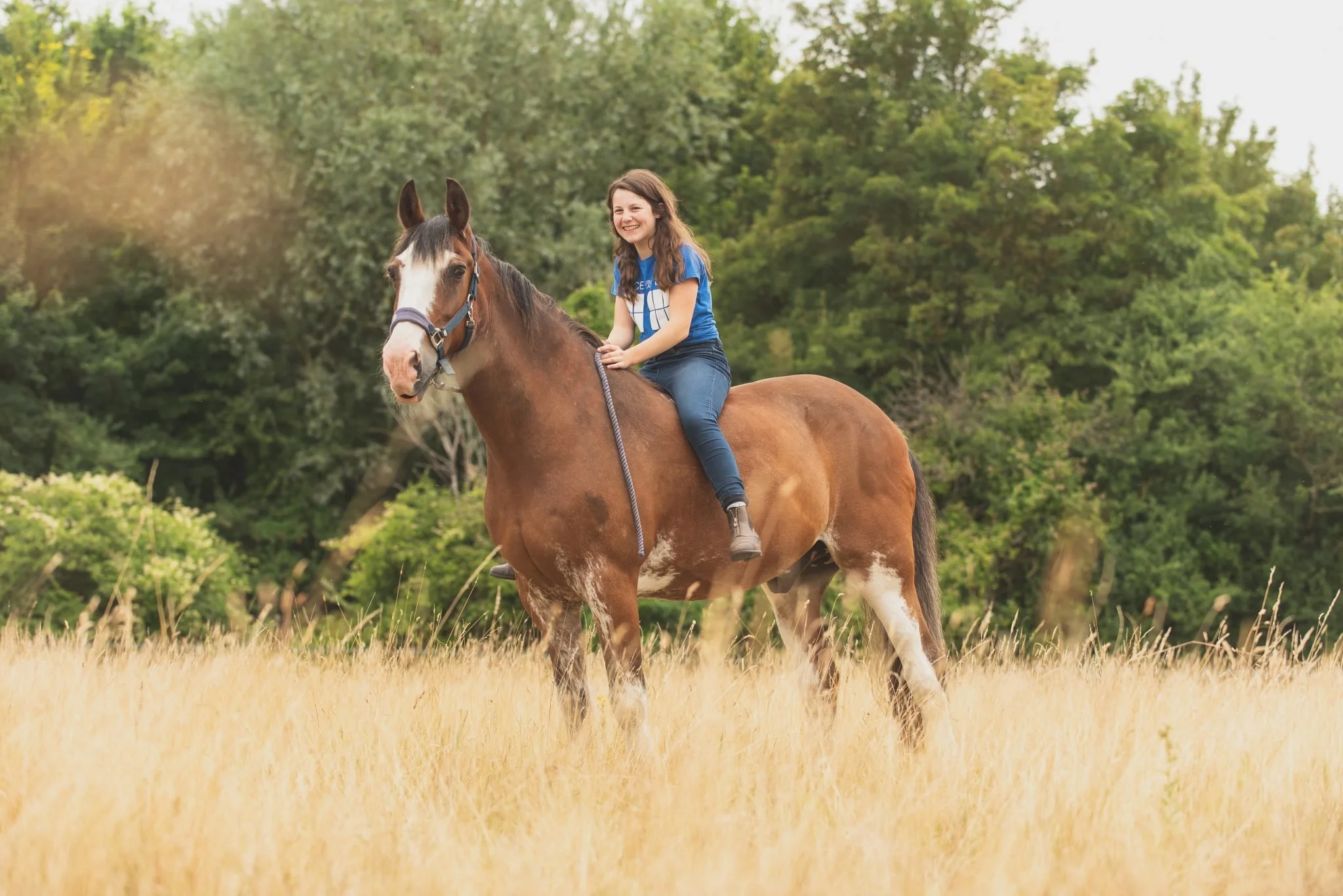A girl riding a brown and white horse in a grassy field with trees in the background.