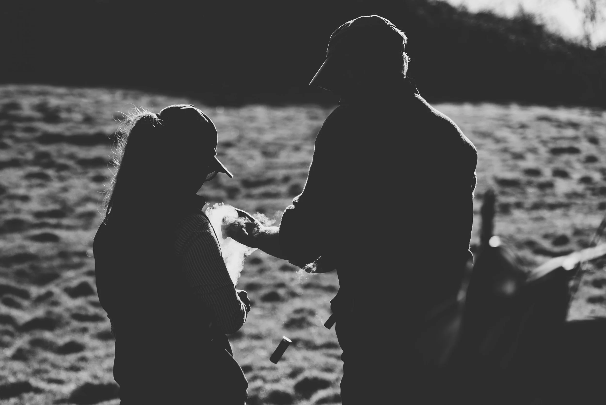 Silhouettes of a man and a girl outdoors, with the man holding a shotgun, in front of the girl. The background shows a blurry, natural setting.
