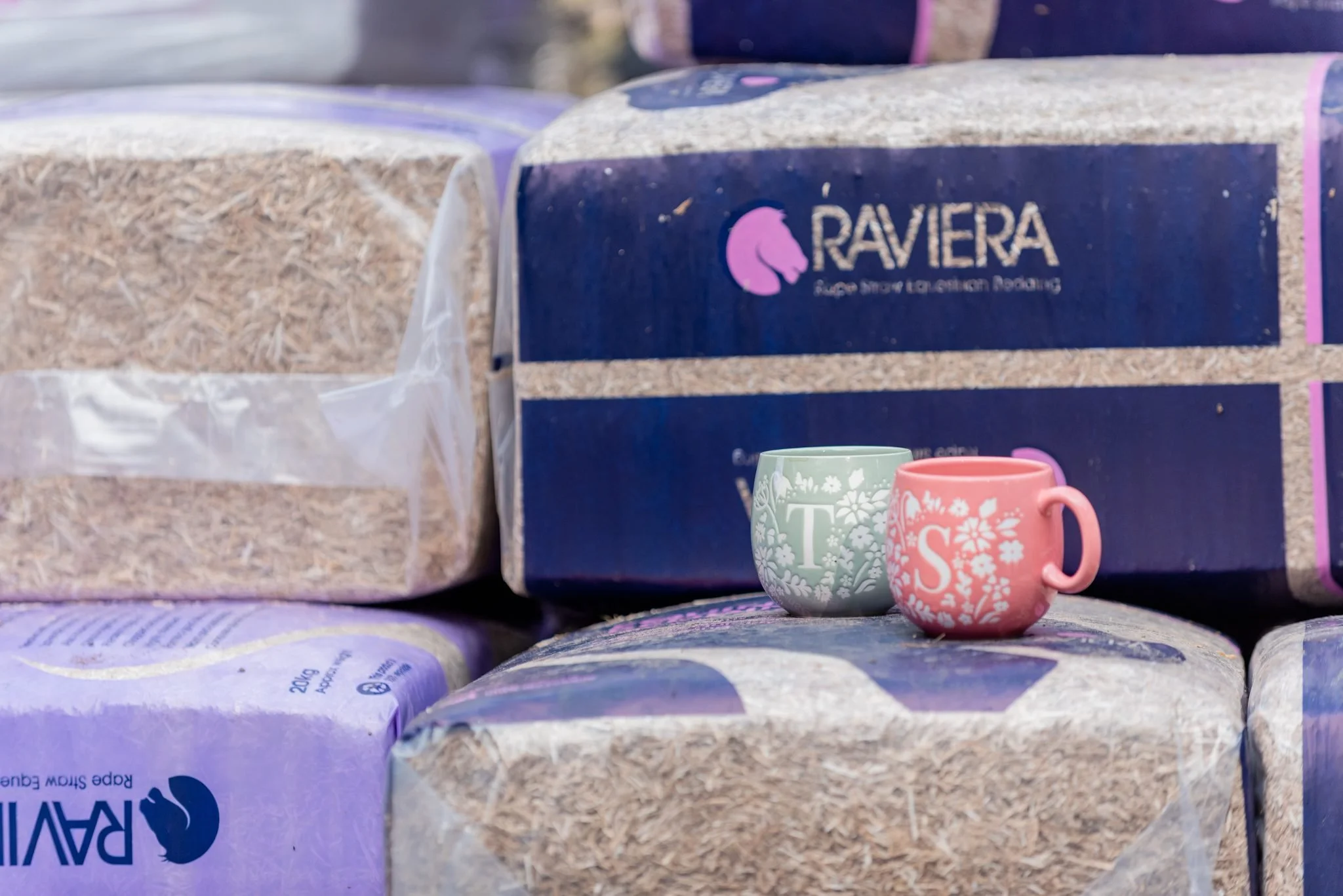 Two floral patterned mugs in pastel colors sitting on a stack of bags of animal bedding, including one labeled 'Raviera' pine shavings.