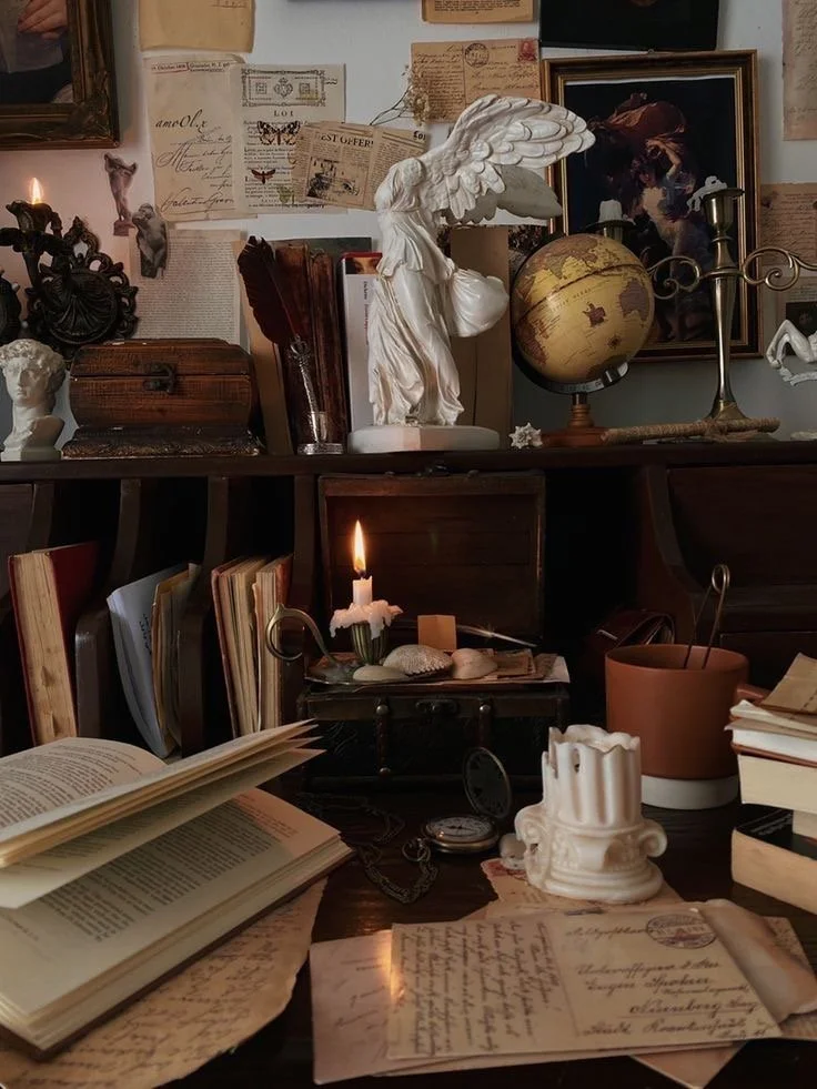 Room with antique decor, books, a globe, a candle, and classical sculptures on the shelves.