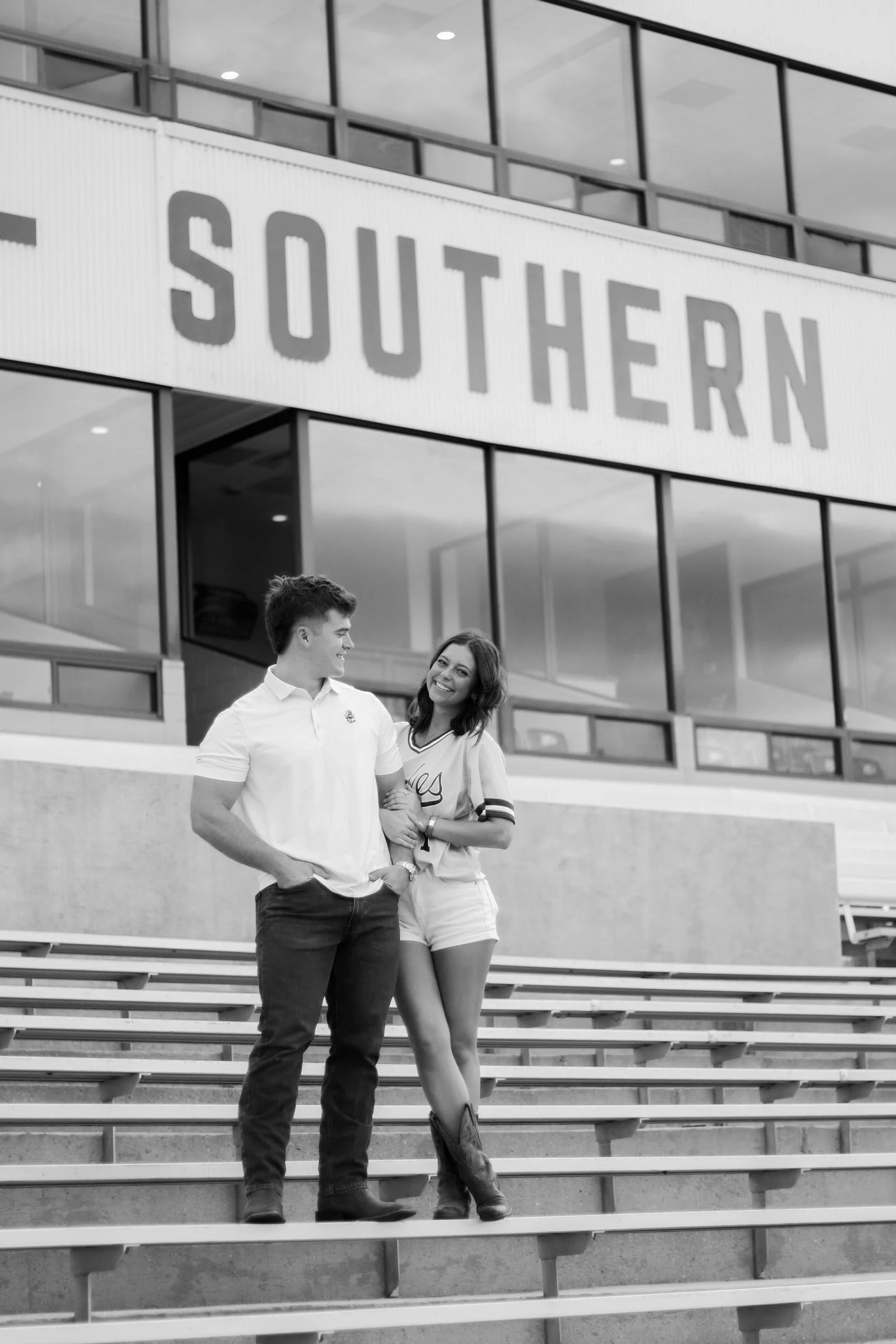 A young man and woman standing on outdoor stairs in front of a modern building with large glass windows and a sign that reads 'SOUTHERN' in capital letters. The man is wearing a white shirt and dark pants, and the woman is wearing a casual t-shirt an