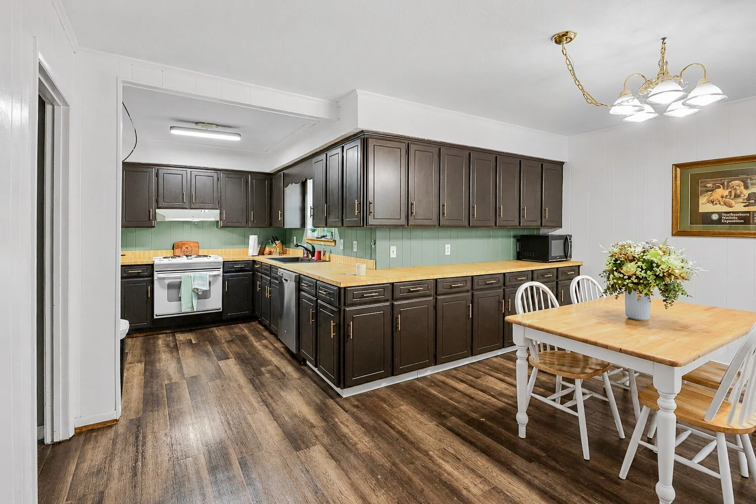 Kitchen with dark wood cabinets, light wood countertops, white walls, and a dining table with a flower arrangement.