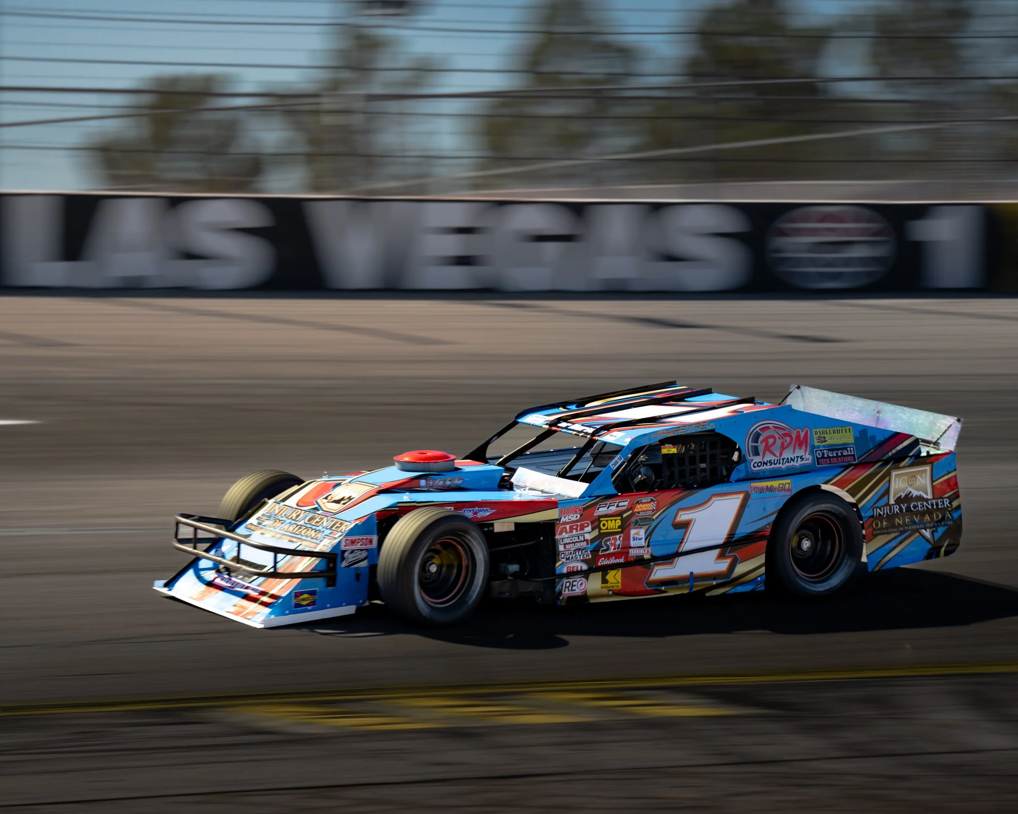 A colorful modified stock car racing around a track with motion blur in the background, featuring various sponsor logos and the number 1 on its side.