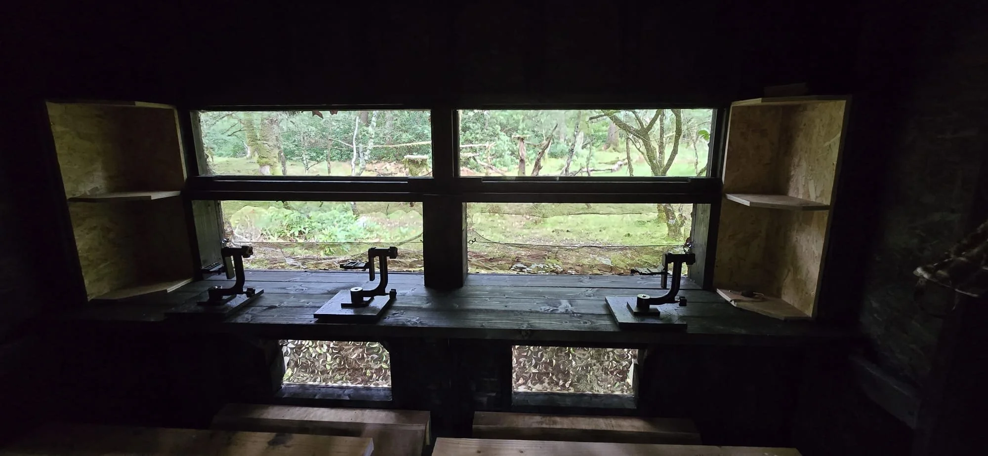 Inside of the Gruline Hide looking out to a woodland area.  Seated viewing area with 4 Gimbals for photography use.  